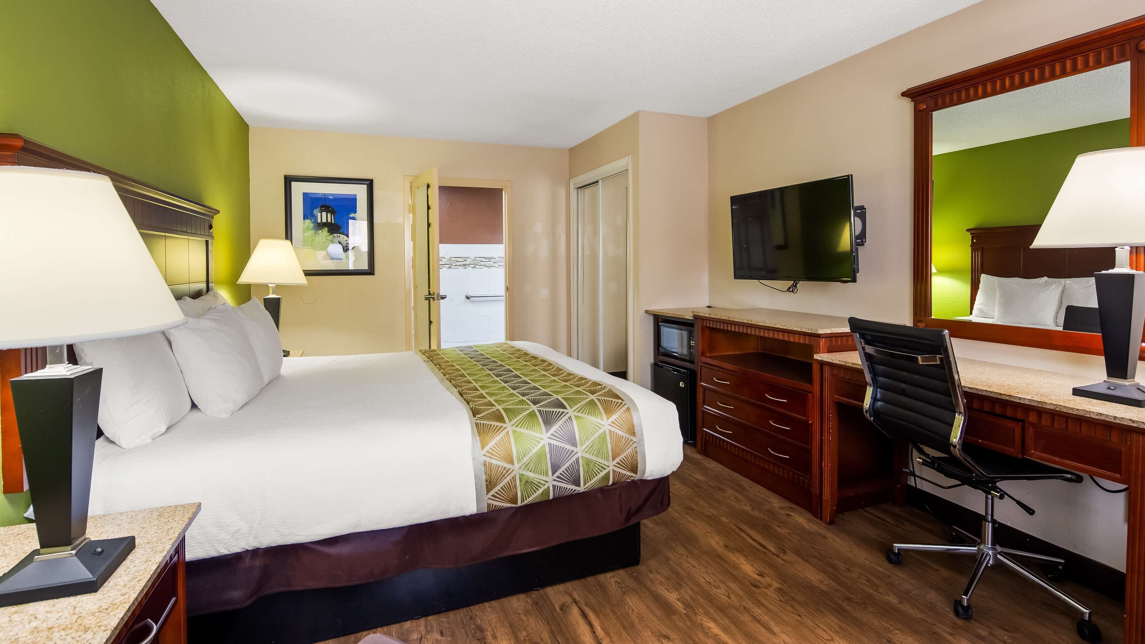 Una habitación de hotel con cama, escritorio, silla, televisión y una puerta que da a un baño.