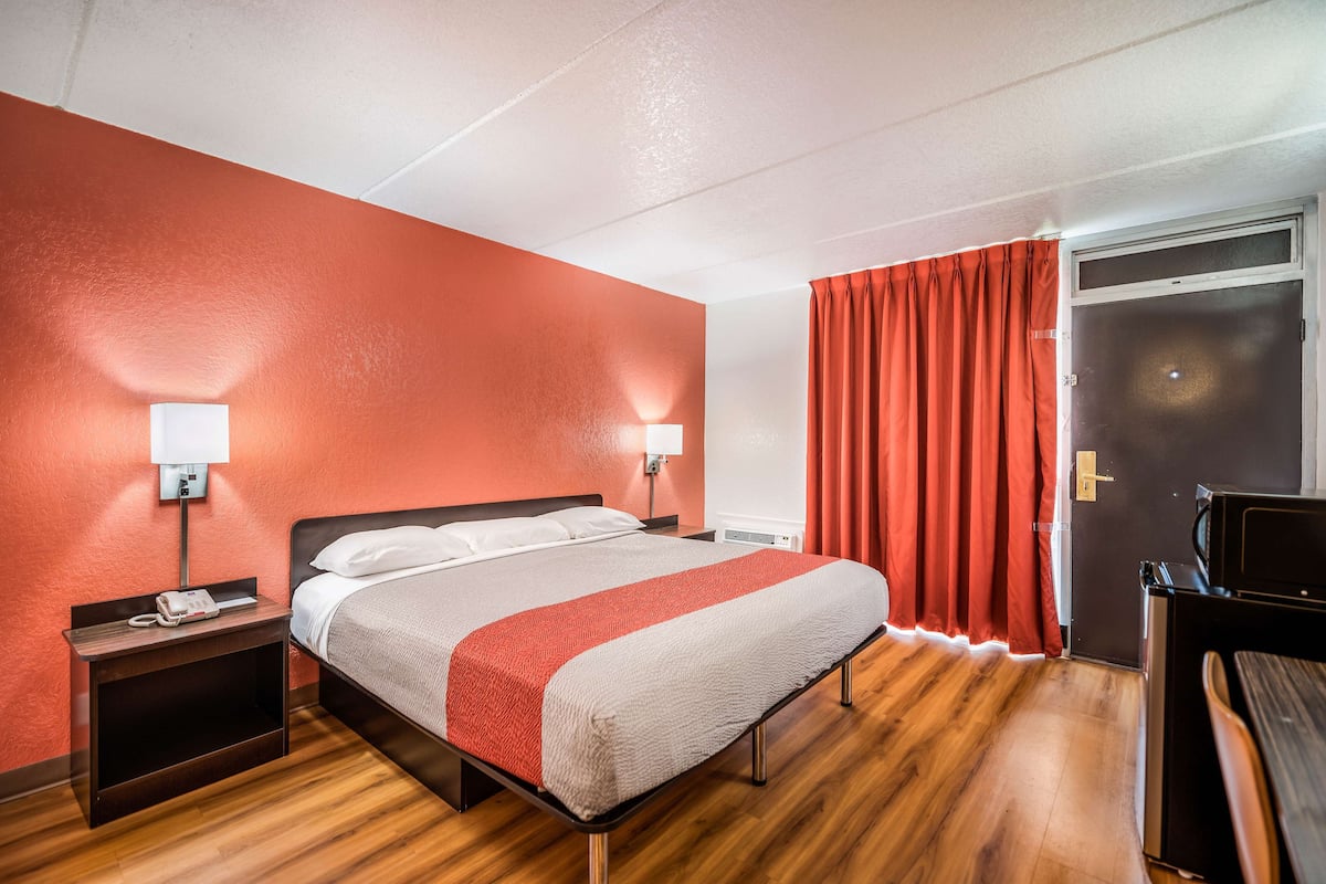 Une chambre d’hôtel avec un lit, des tables de chevet, un bureau et une porte.