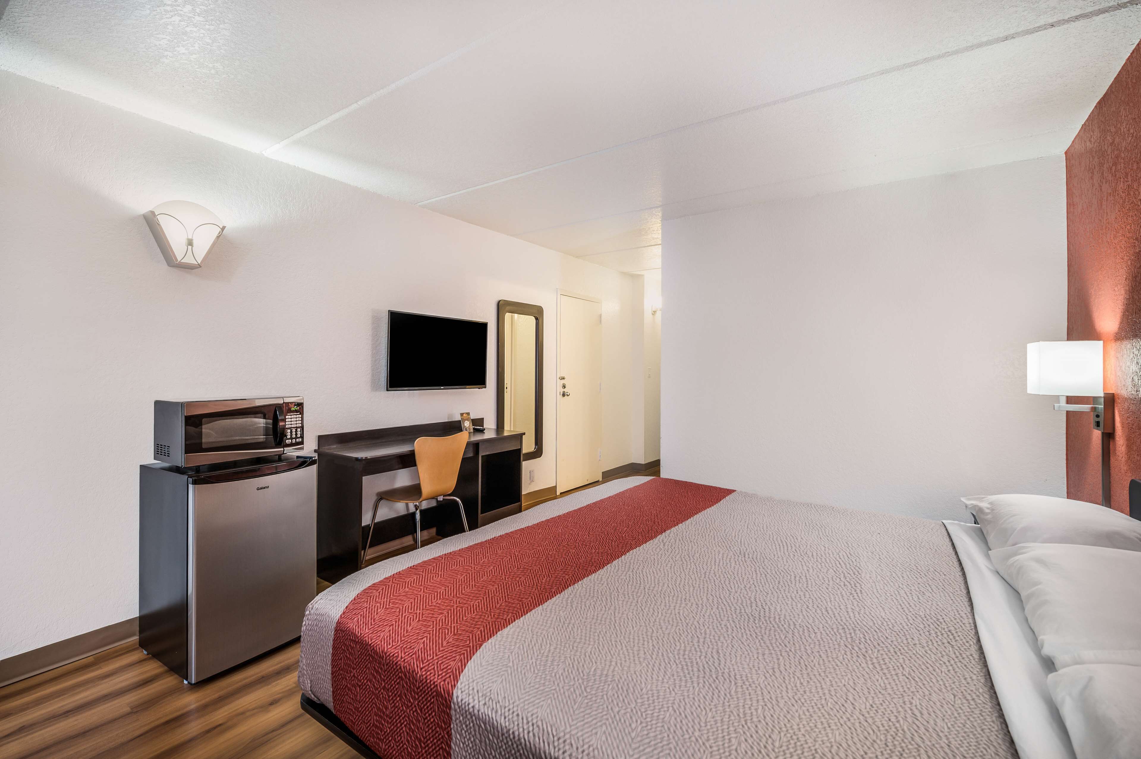 A hotel room with a bed, a desk with a microwave, a chair, and a television on the wall.