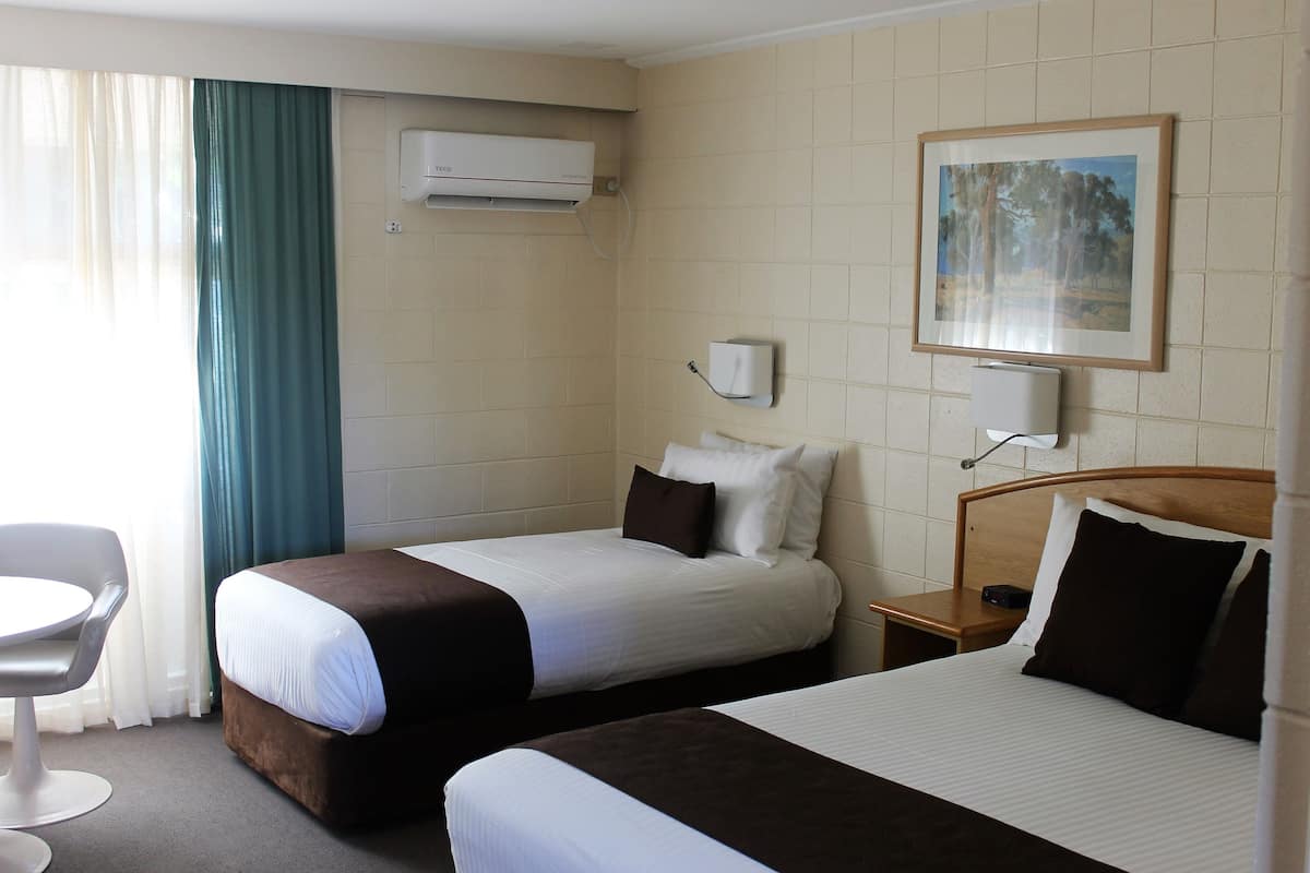 Et hotelværelse med to senge, et skrivebord, en stol, en aircondition og et billede på væggen.