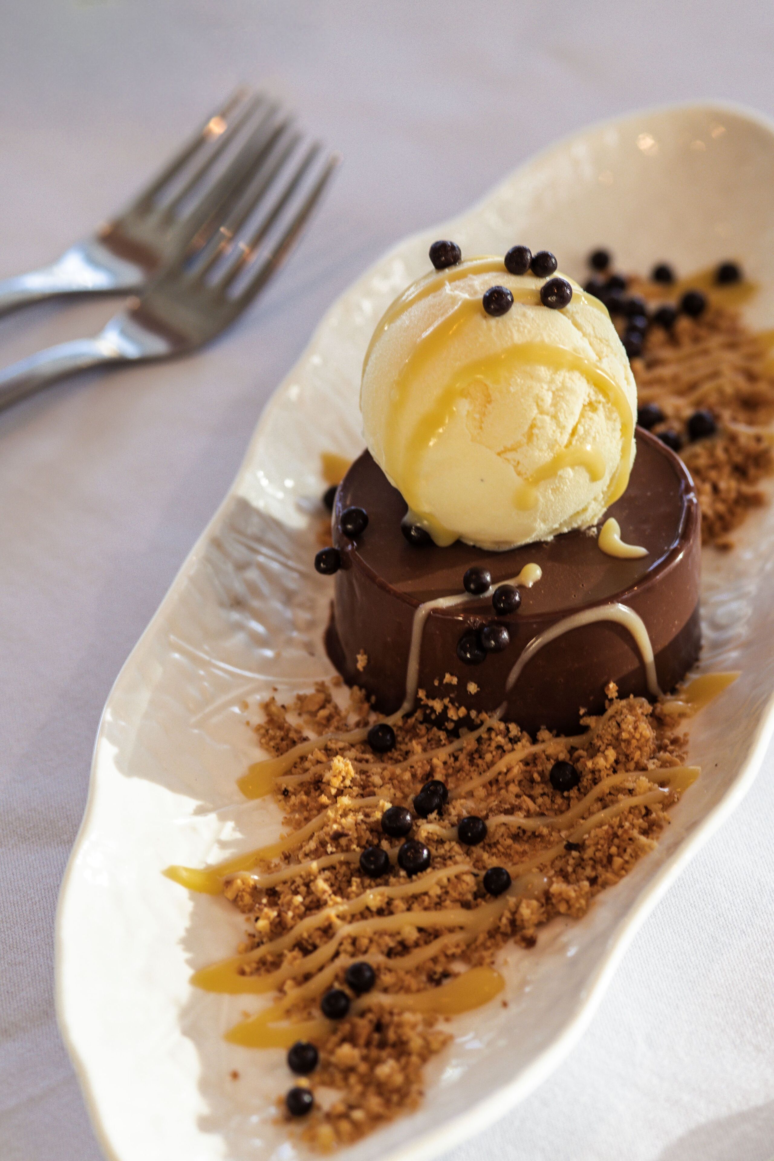 Un postre sobre un plato blanco con detalles de chocolate y caramelo, acompañado de un tenedor.
