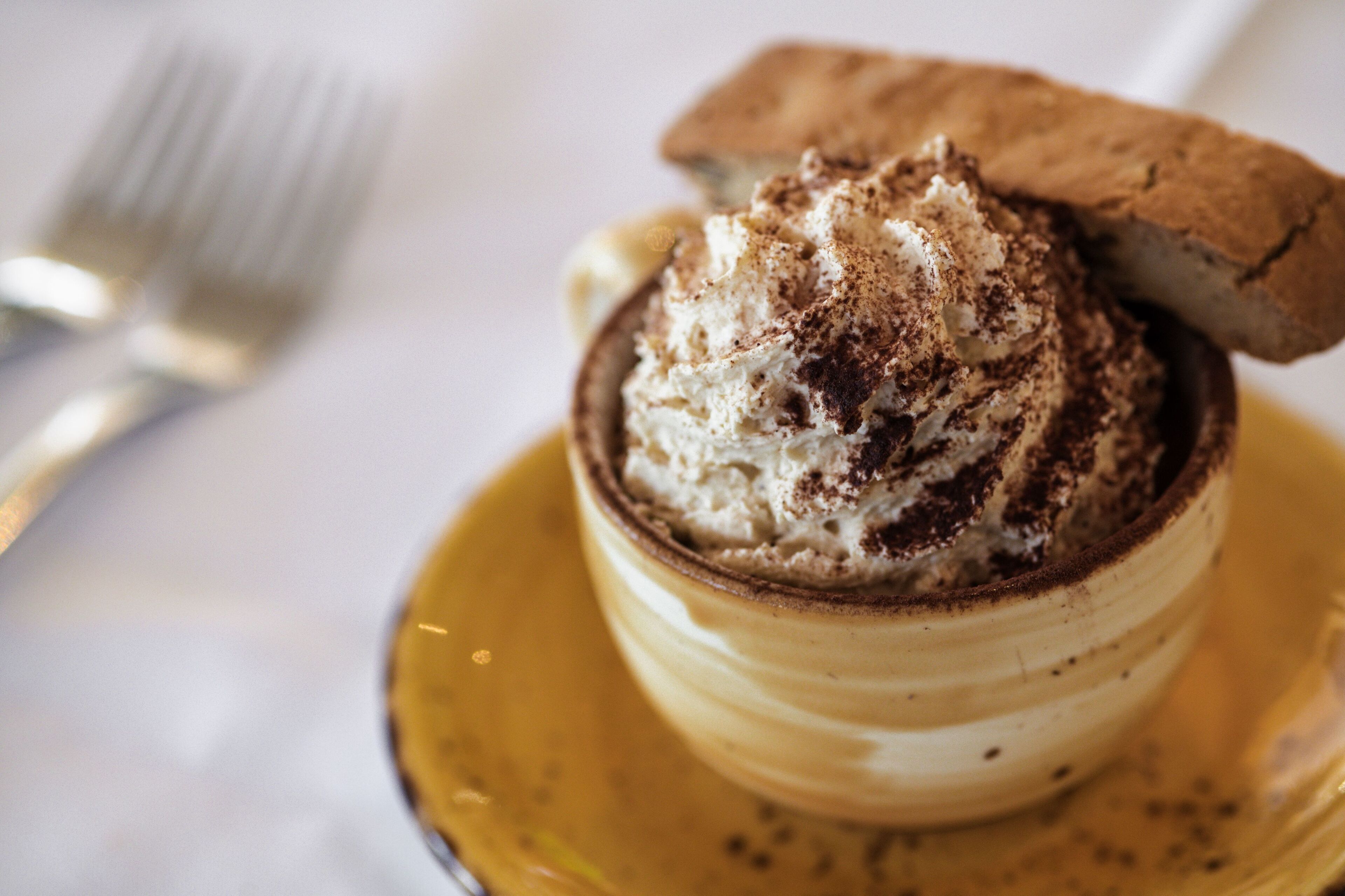 A dessert with whipped cream and a cookie on top, served in a yellow cup on a saucer.