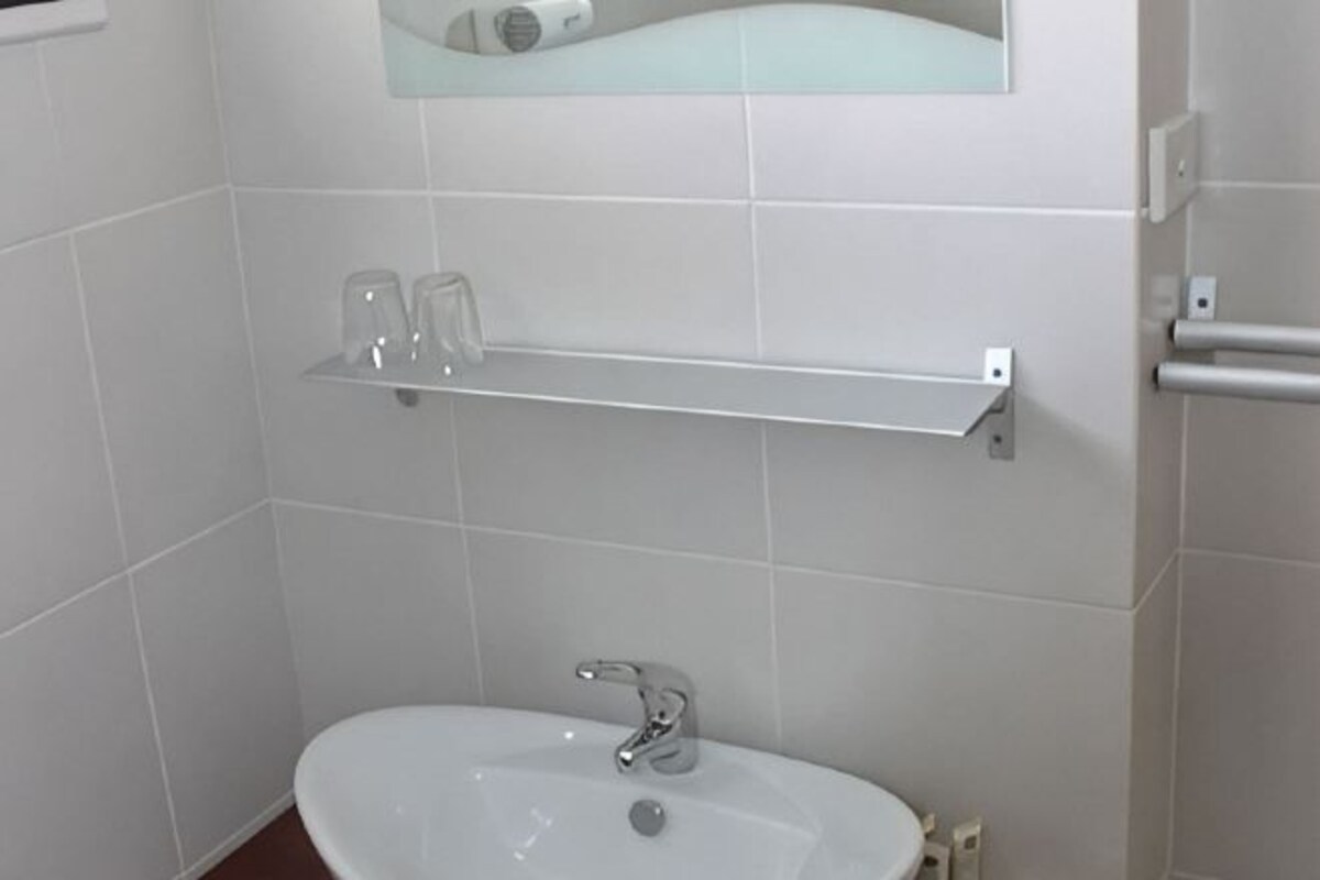 A bathroom with a white sink, a mirror above it, and a shelf with two glasses.