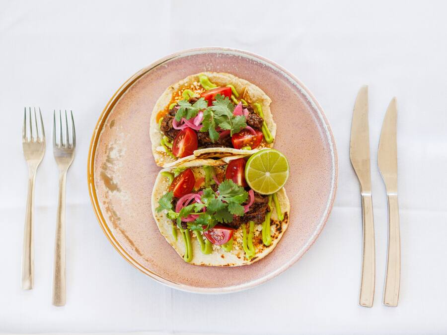 Un plato con dos tacos, una cuña de limón y una cuchara.