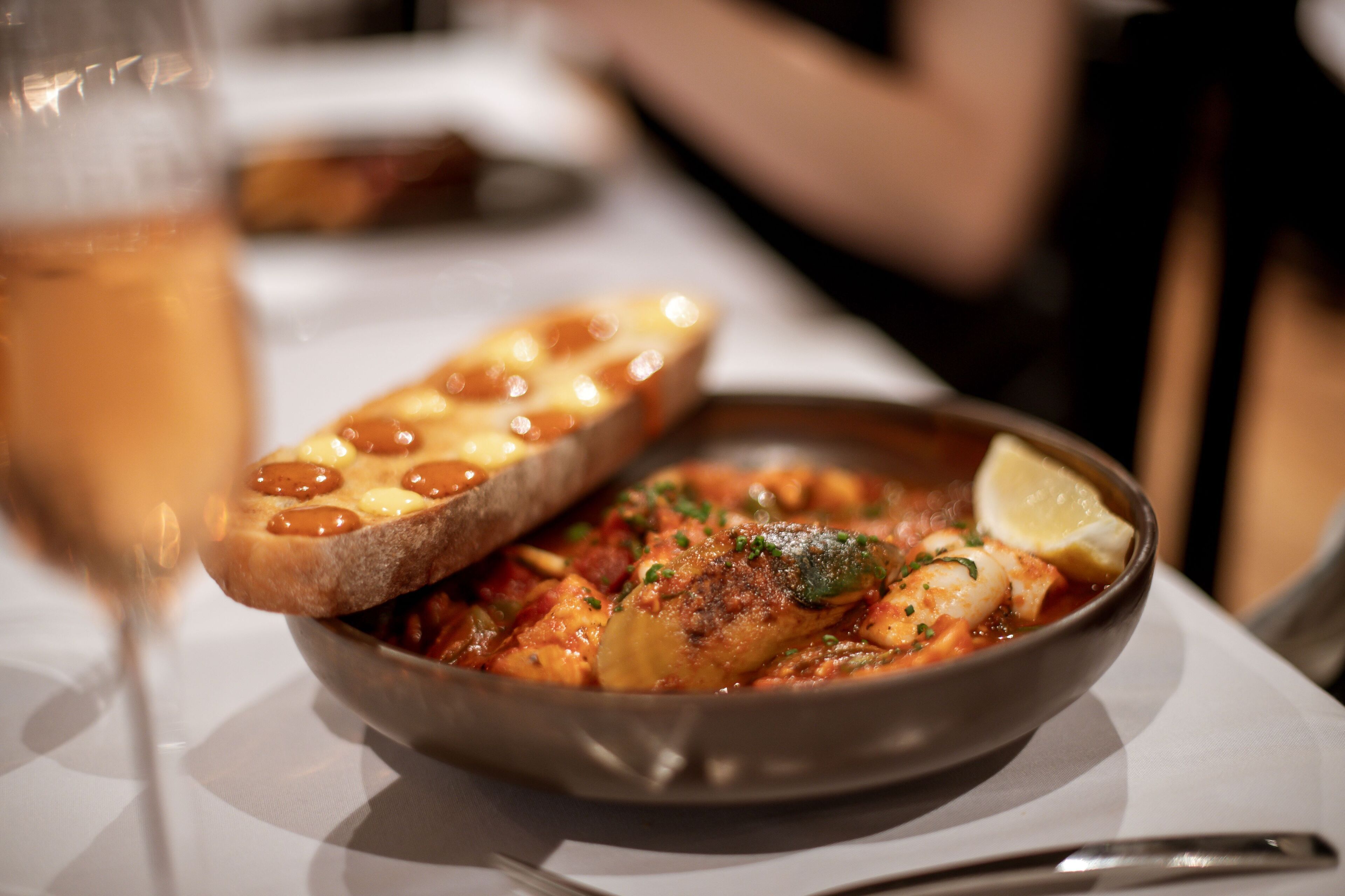 En skål med pastarätt med skaldjur, garnerad med en citronskiva, på ett vitt bord.