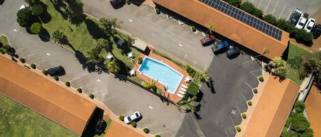 An aerial view of a hotel with a swimming pool surrounded by parking spaces and greenery.