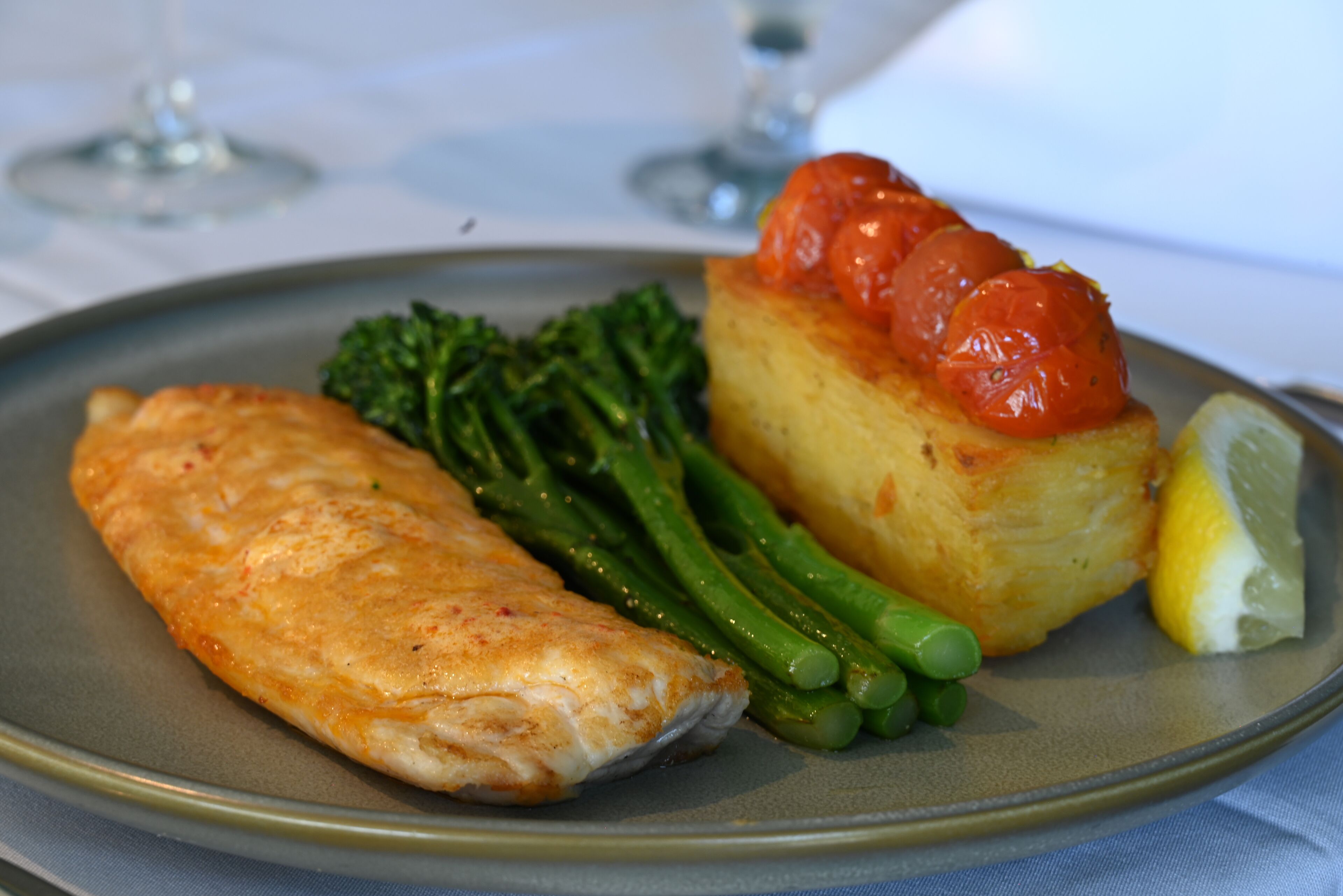 A plate with a piece of fish, green beans, a baked potato topped with tomatoes, and a lemon wedge.