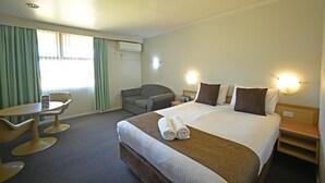Een hotelkamer met een groot bed, een bureau met stoel, een bank en een raam met gordijnen.