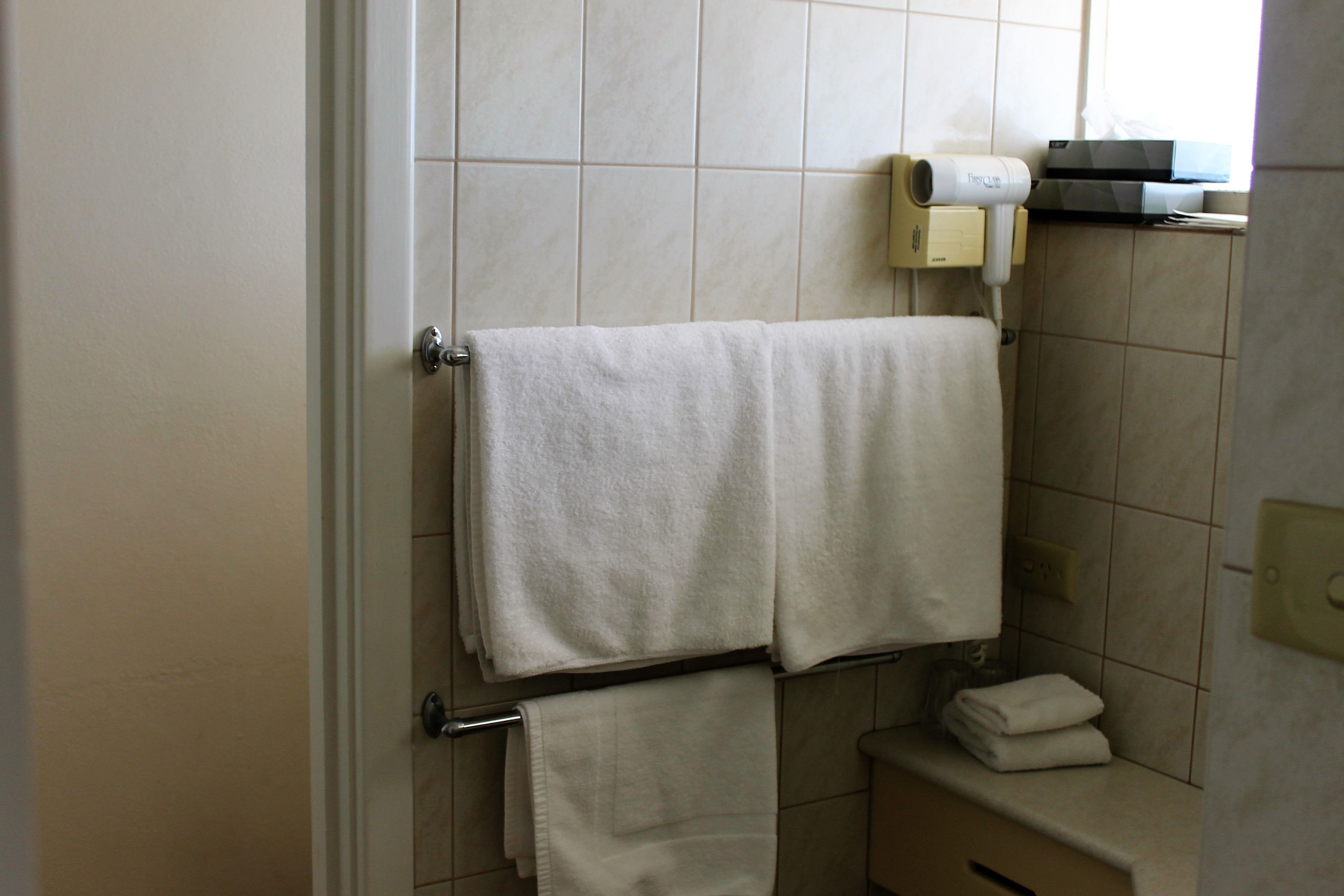 A bathroom with a towel rack holding two towels, a small sink with a mirror, and a towel dispenser on the wall.