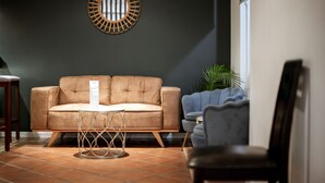 Een moderne woonkamer met een bruine leren bank, een kleine ronde spiegel en een blauwe fauteuil.