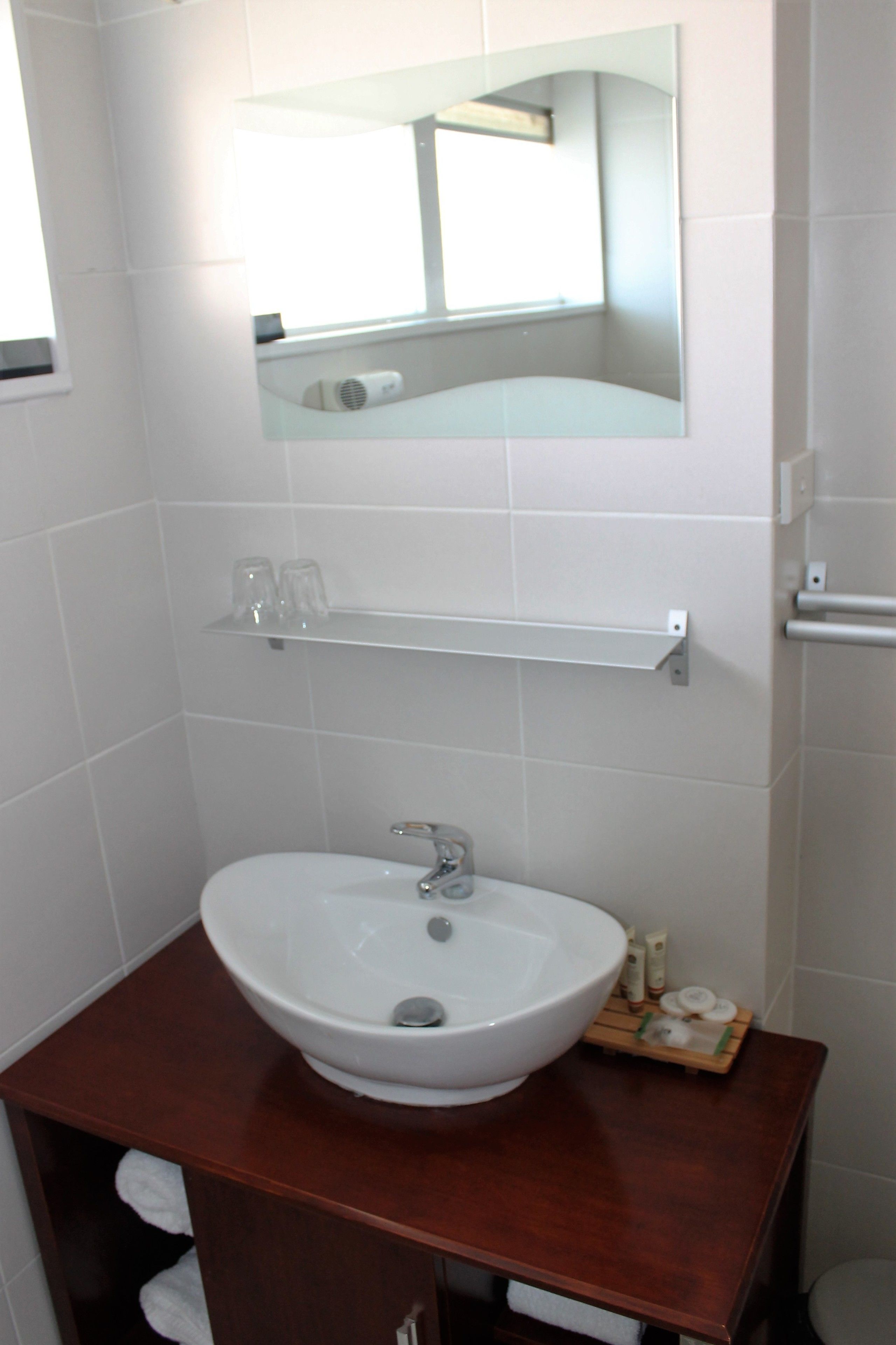 A bathroom with a white sink, a mirror above it, and a shelf with toiletries.