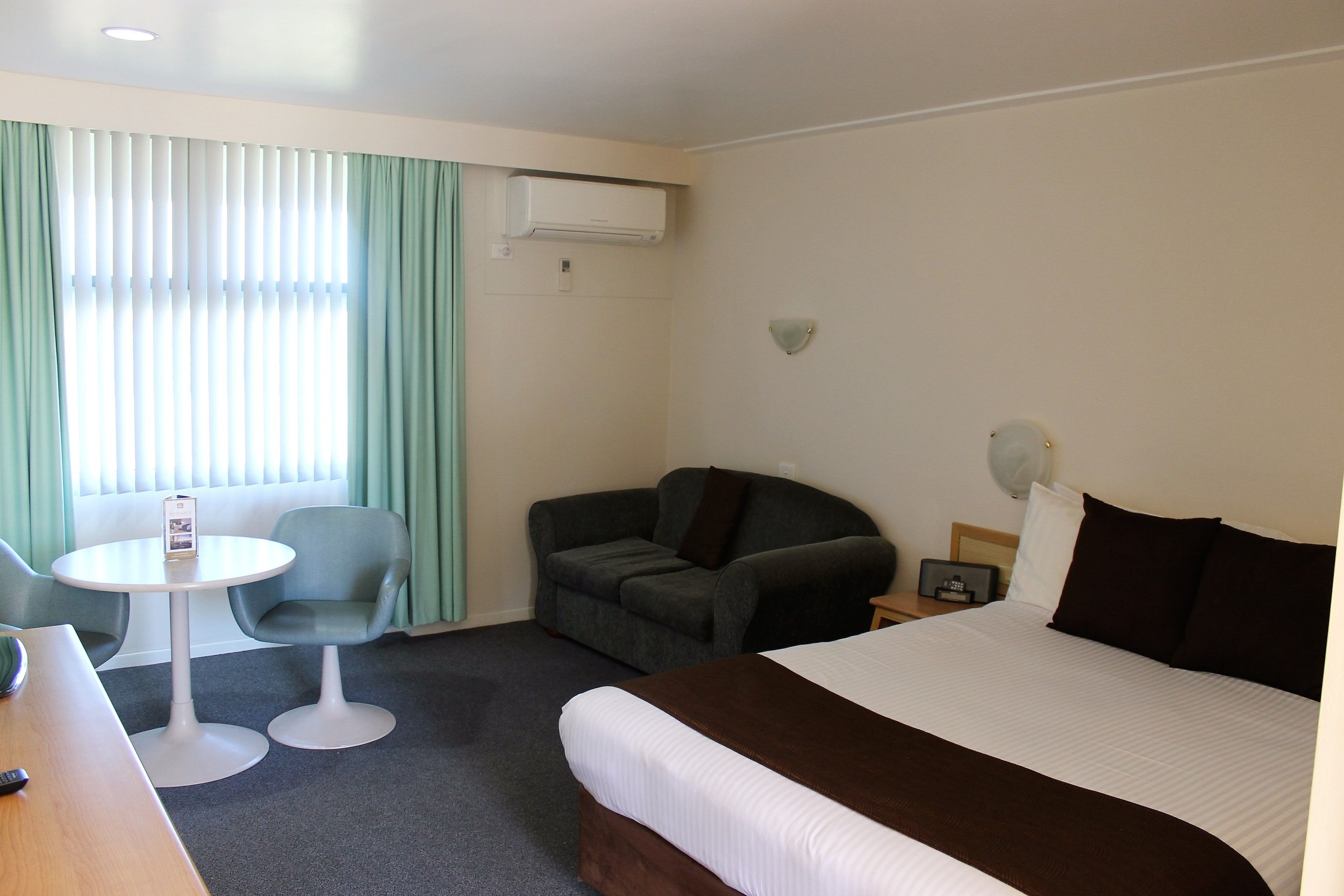 A hotel room with a bed, a desk, two chairs, a small table, and a window with curtains.
