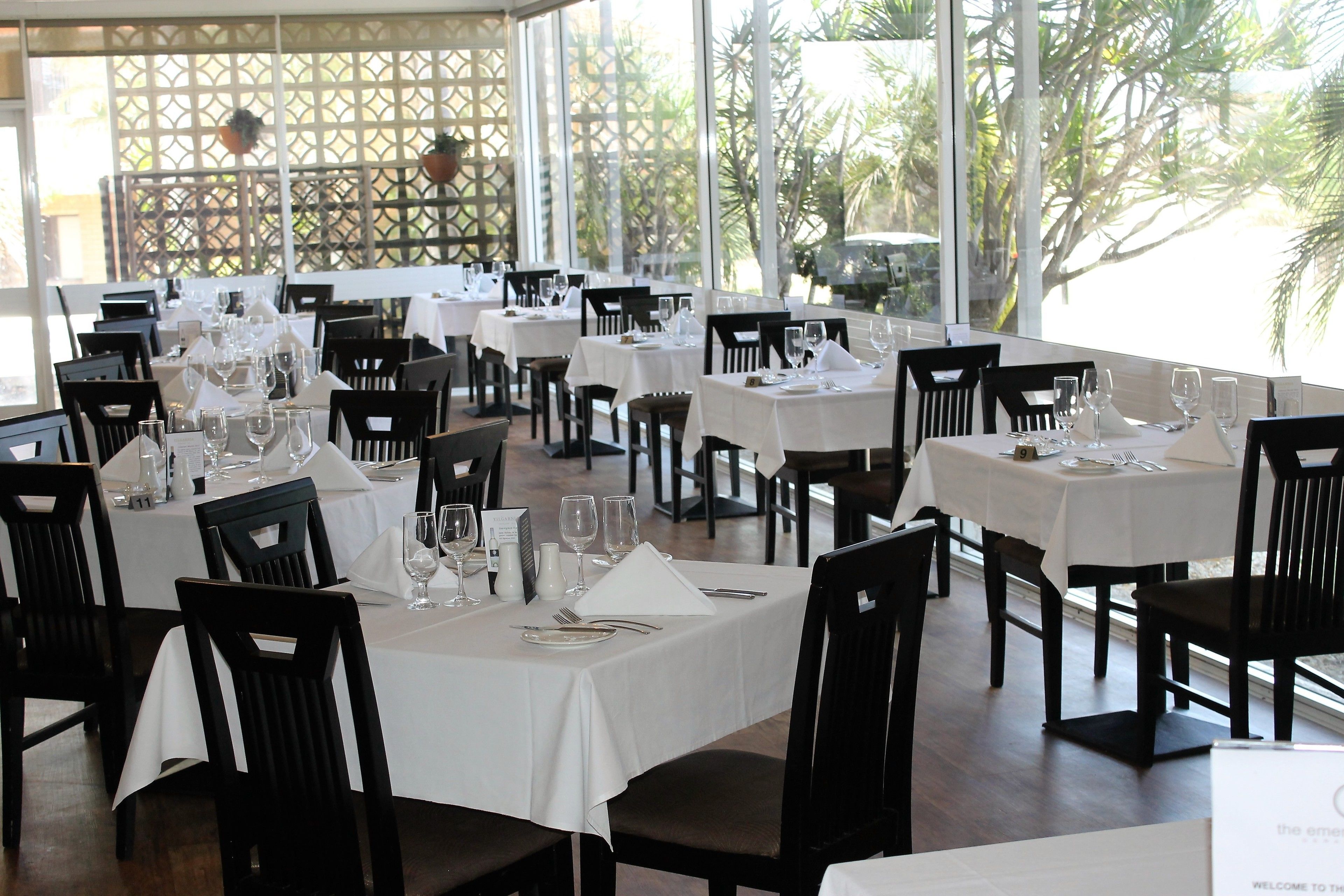 A restaurant with multiple tables set for dining, featuring white tablecloths and black chairs.