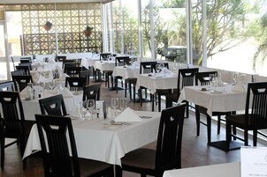 Un restaurante con varias mesas preparadas para comer, con manteles blancos y sillas negras.