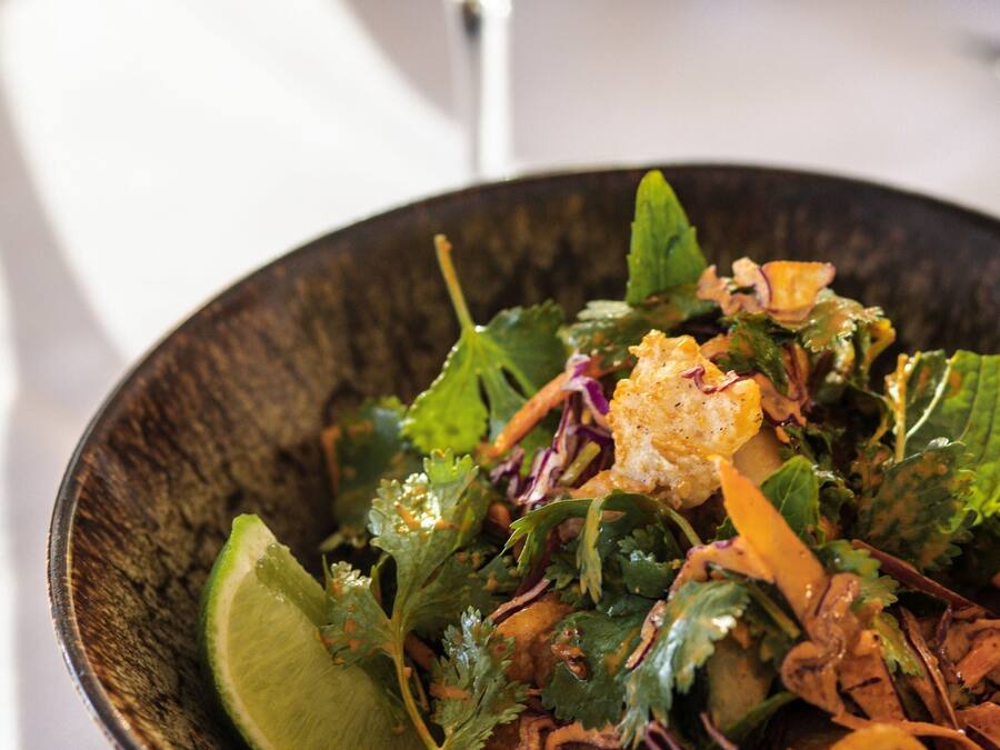 Uma salada com diversos ingredientes e um copo de vinho branco sobre uma mesa.