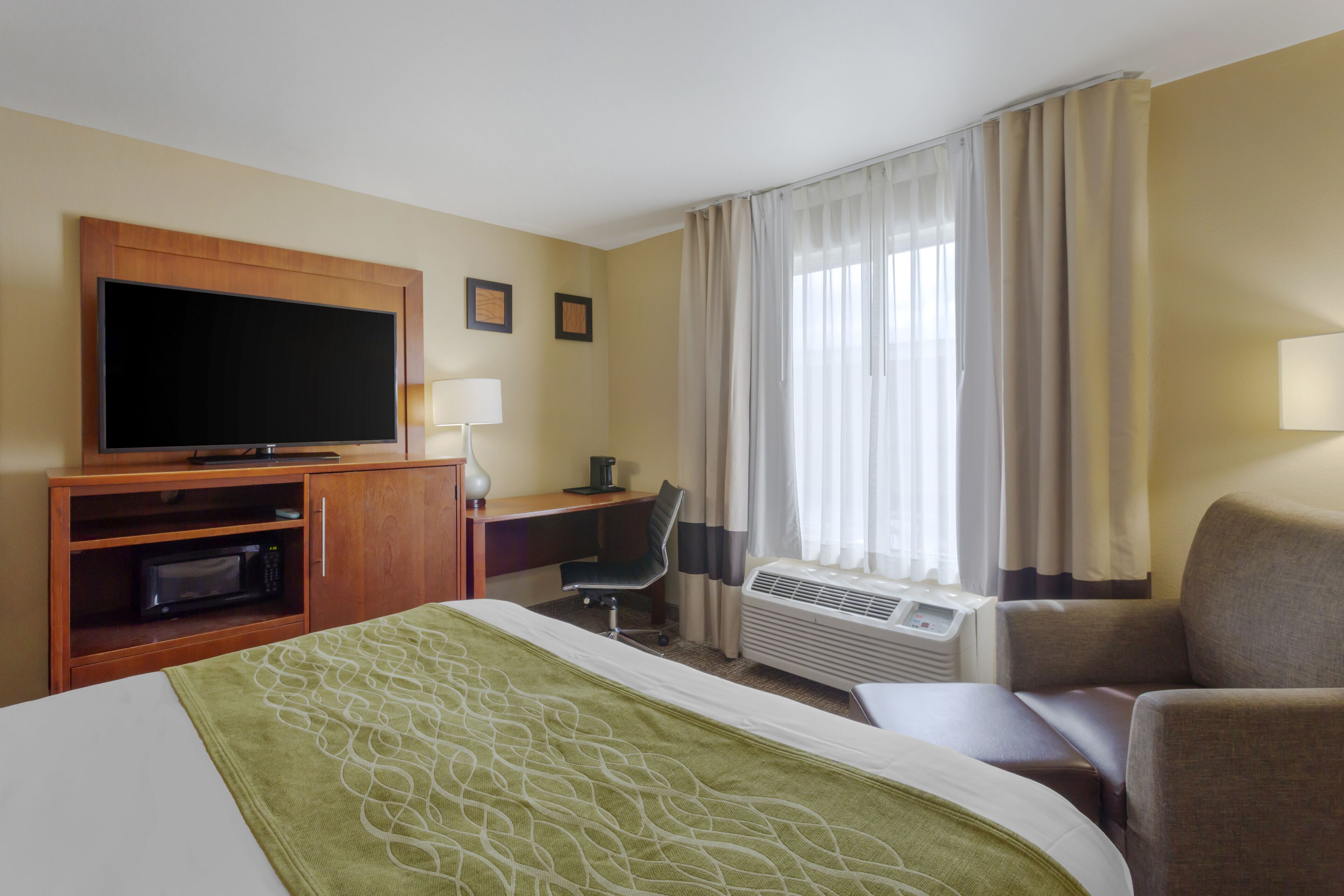 Habitación de hotel con cama, escritorio, televisión, aire acondicionado y una silla.
