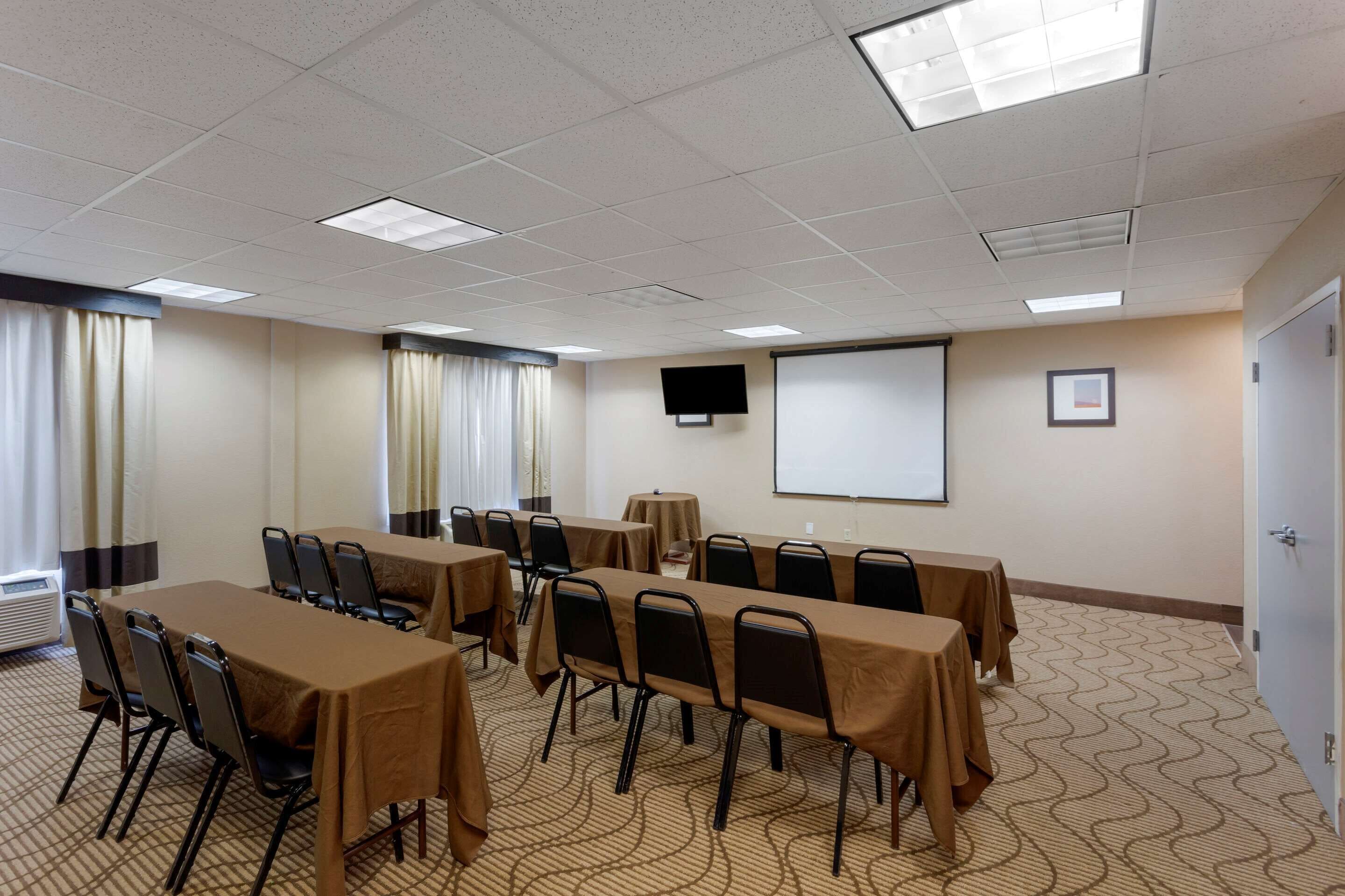 A conference room with tables and chairs, a projector screen, and a flat-screen TV on the wall.