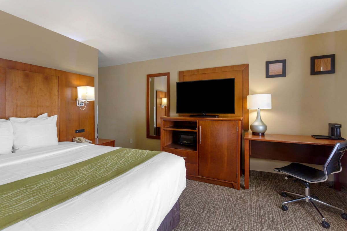 Ein Hotelzimmer mit einem großen Bett, einem Schreibtisch mit Stuhl, einem Fernseher und einer Lampe.