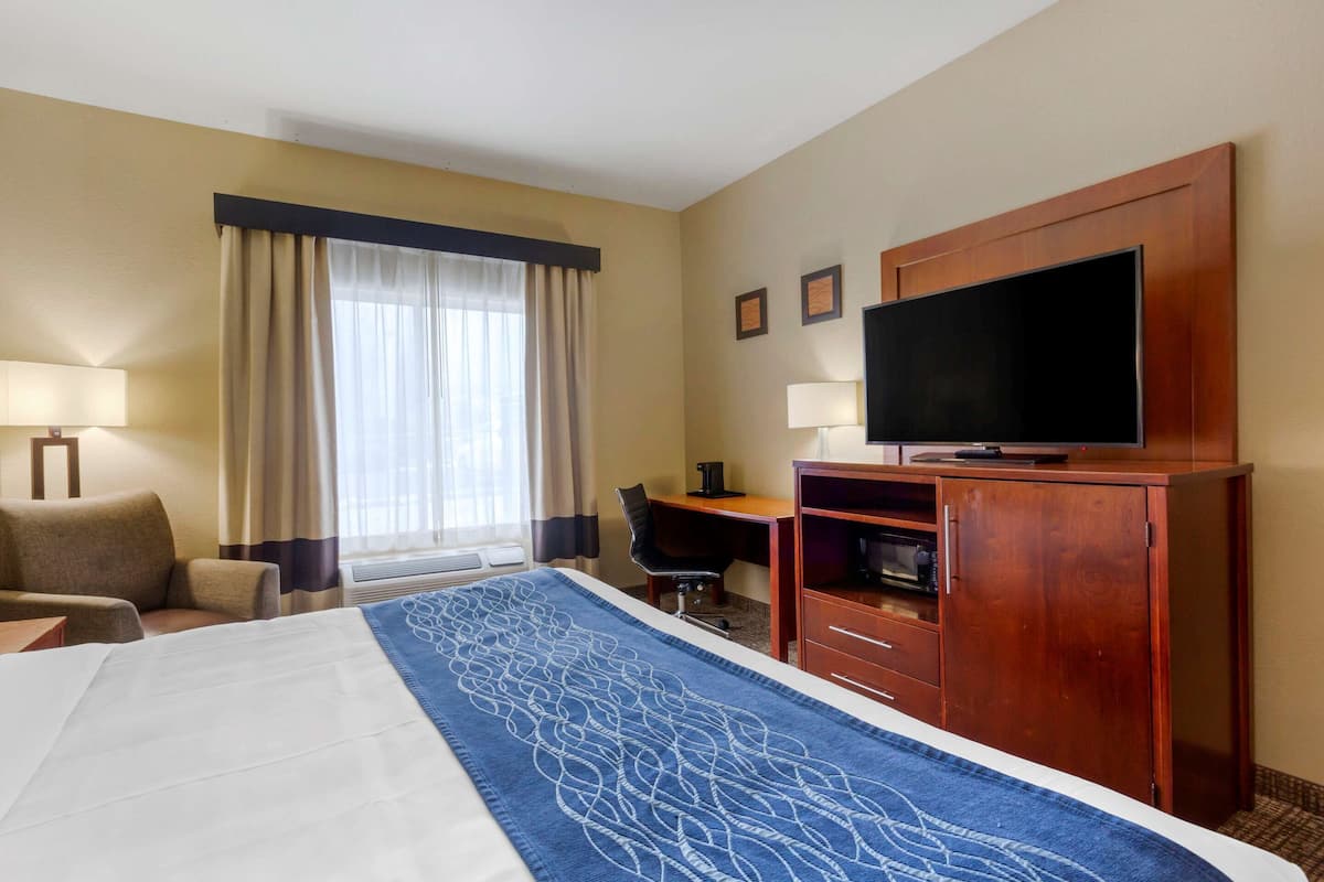 Ein Hotelzimmer mit einem großen Bett, einem Schreibtisch mit Stuhl, einem Fernseher und einem Kleiderschrank.