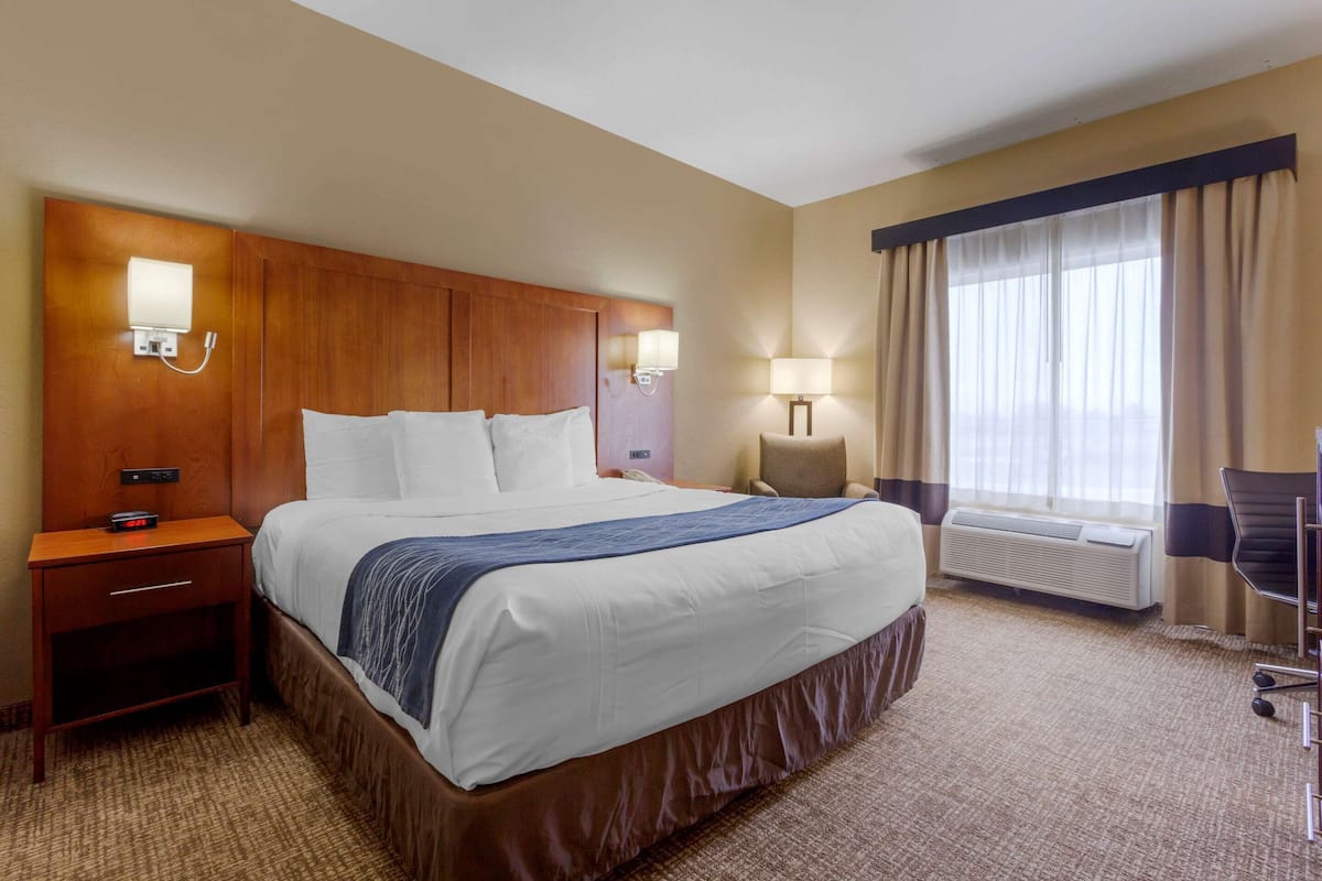 Ein Hotelzimmer mit einem großen Bett, einem Holzkopfteil, Nachttischlampen, einem Schreibtisch und einem Sessel.