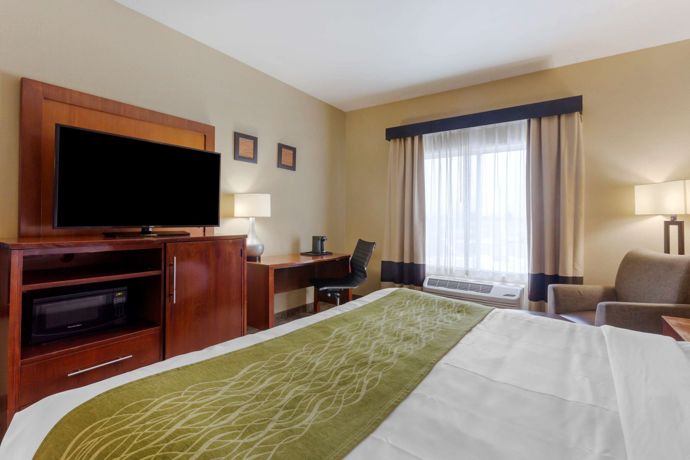 Een hotelkamer met een bed, een televisie, een bureau, een stoel en een raam met gordijnen.