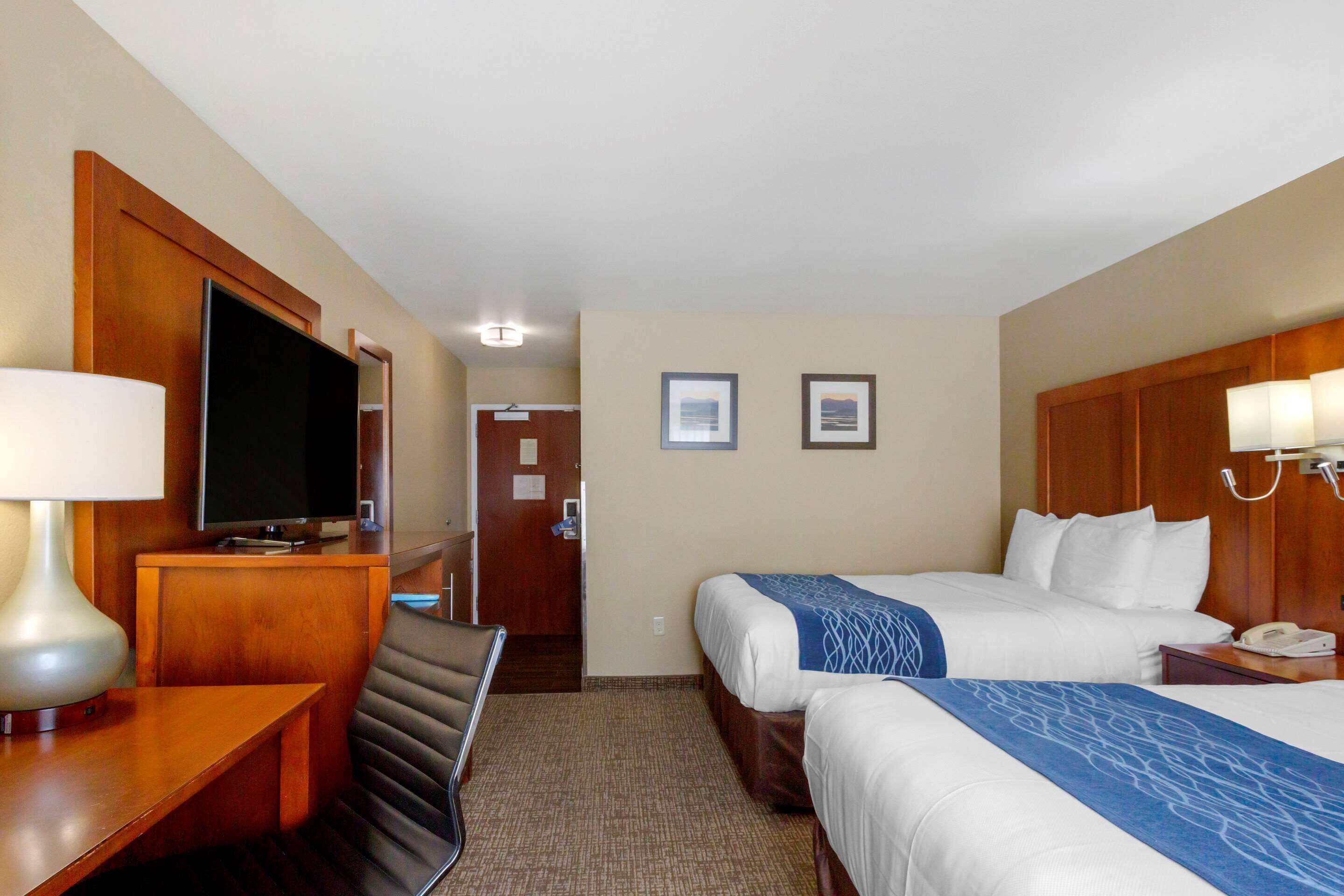 A hotel room with two beds, a desk with a lamp, a television, and framed pictures on the wall.