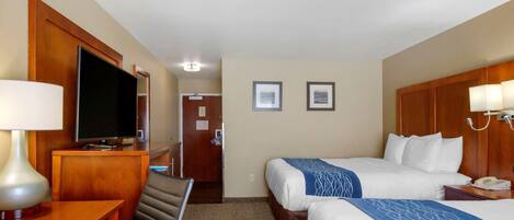 A hotel room with two beds, a desk with a lamp, a television, and framed pictures on the wall.