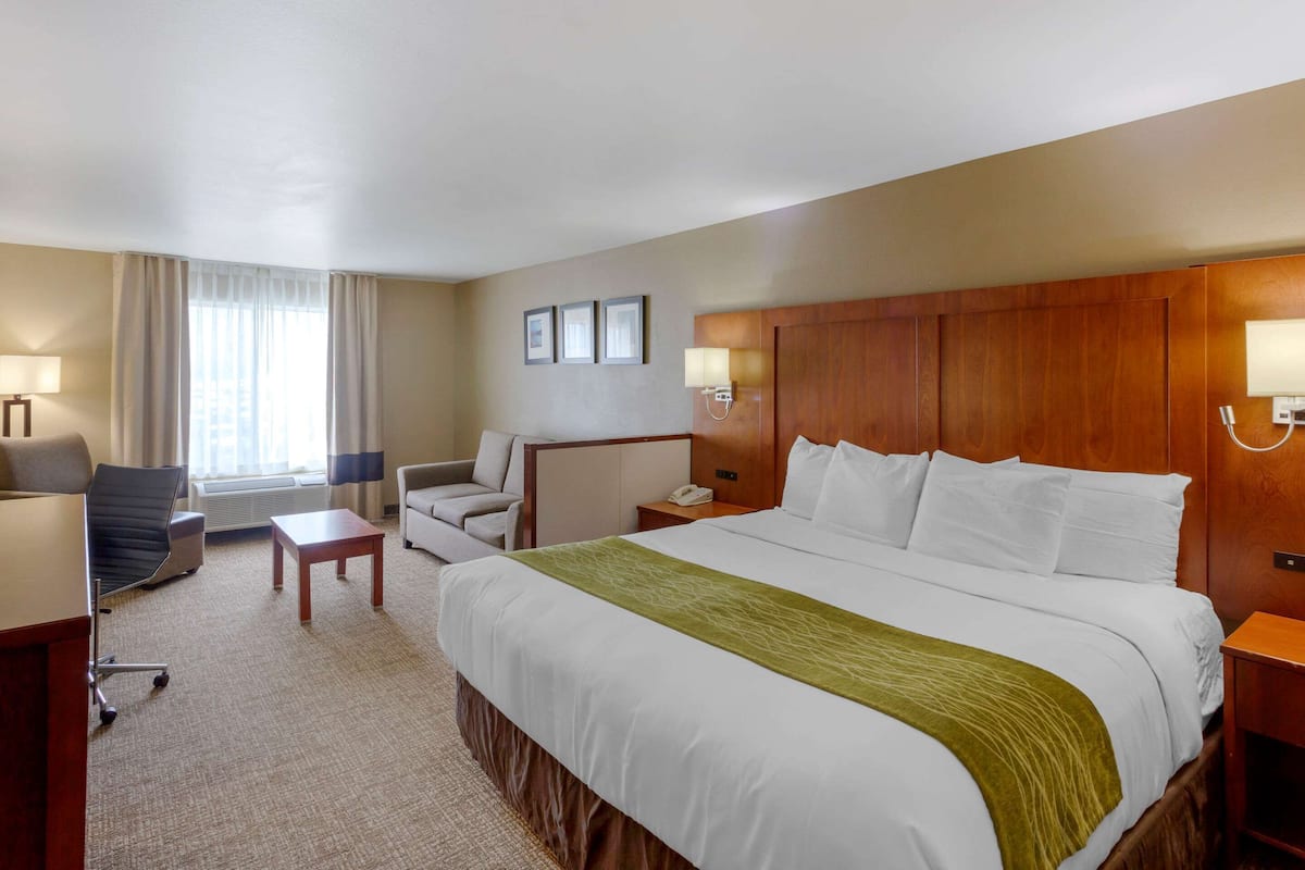 Ein Hotelzimmer mit einem großen Bett, einem Schreibtisch, einem Stuhl, einem kleinen Tisch und einer Lampe.