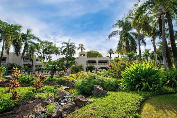 Un resort con piscina, palmeras y un edificio con varios balcones.