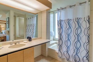A bathroom with a large mirror, a sink, a bathtub, and a shower curtain with a wavy pattern.