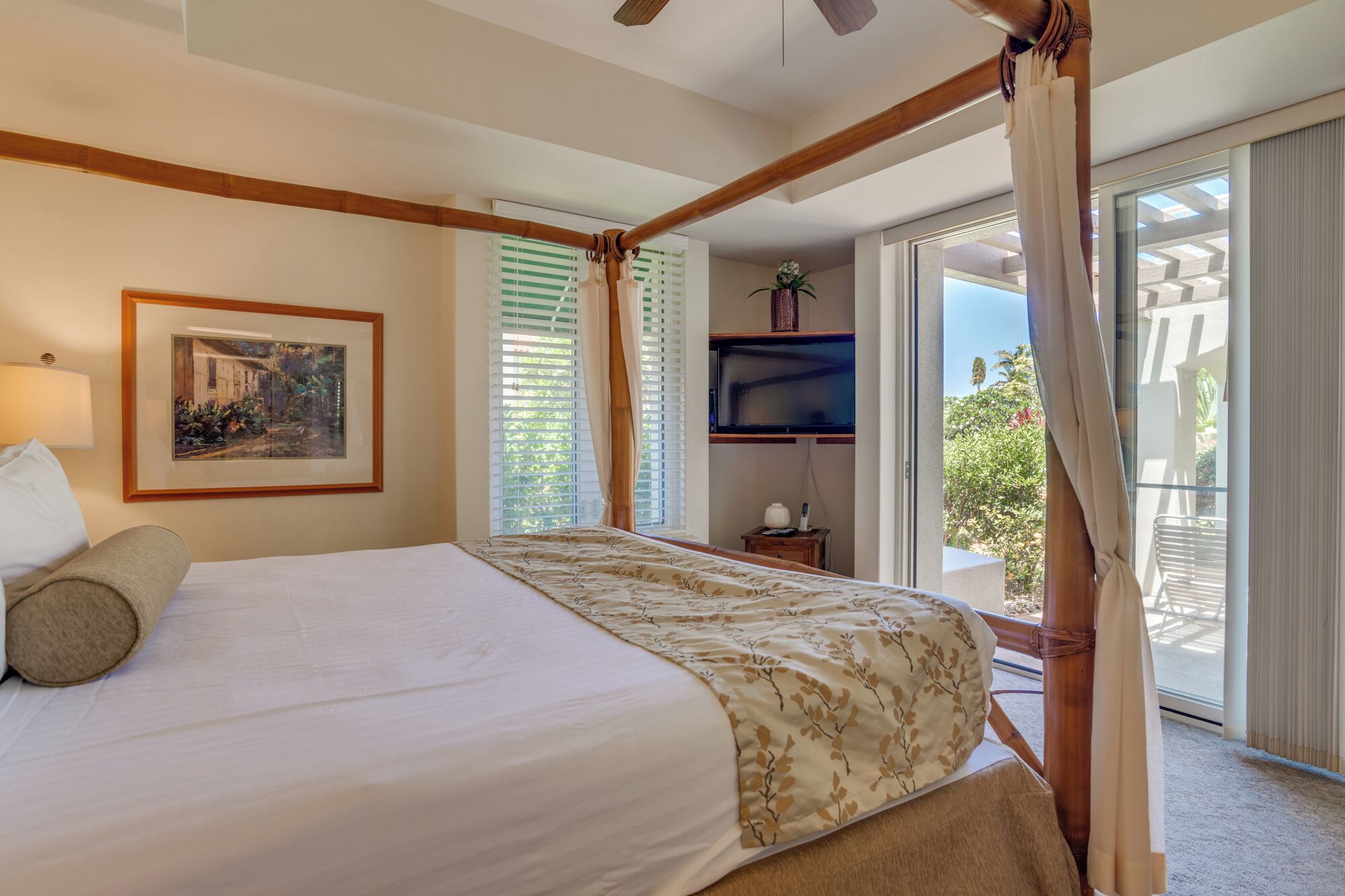 Un dormitorio con cama, un cuadro enmarcado, televisión y balcón con cortinas.