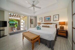 A hotel room with a bed, a bench, a TV, a ceiling fan, and a view of the outdoors. - Palms at Wailea Maui (Kihei)