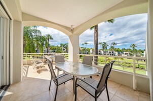 A covered outdoor area with a round table and chairs, a view of palm trees and buildings, and a white railing.