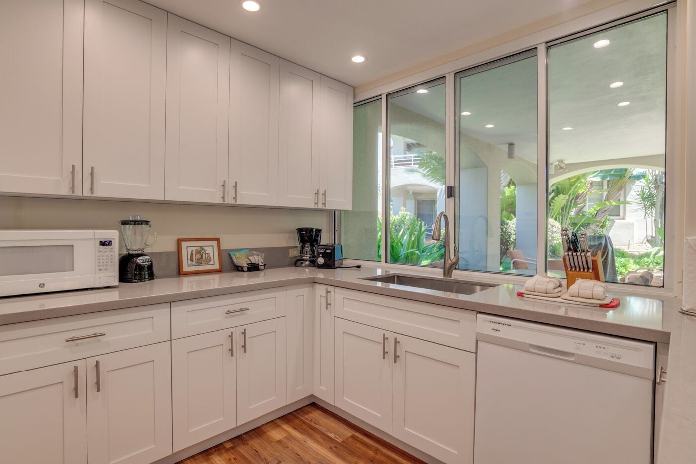 A modern kitchen with white cabinets, a microwave, a coffee maker, and a sink.