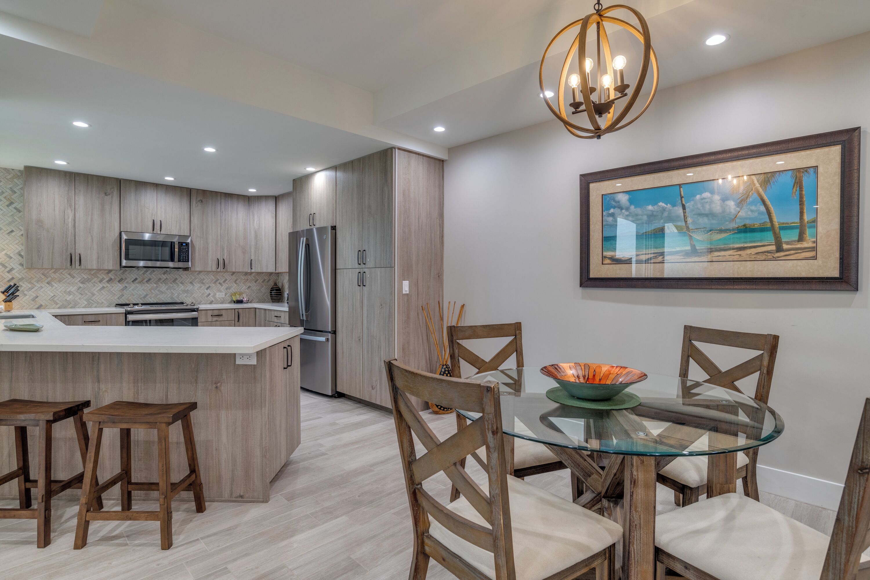 A modern kitchen with wooden cabinets, a central island with stools, and a dining area with a glass table and chairs.