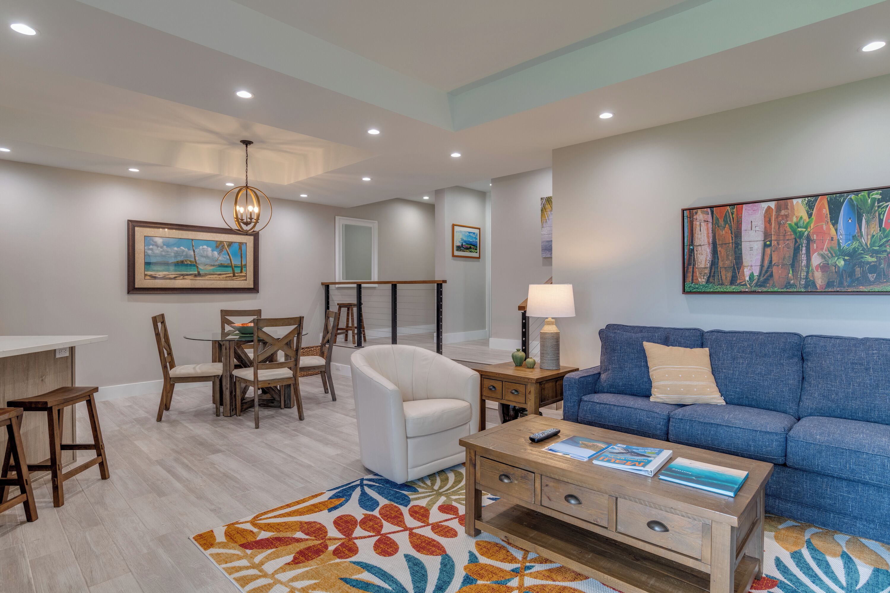 Una sala de estar moderna con un sofá azul, un sillón blanco, una mesa de centro de madera y una alfombra colorida.