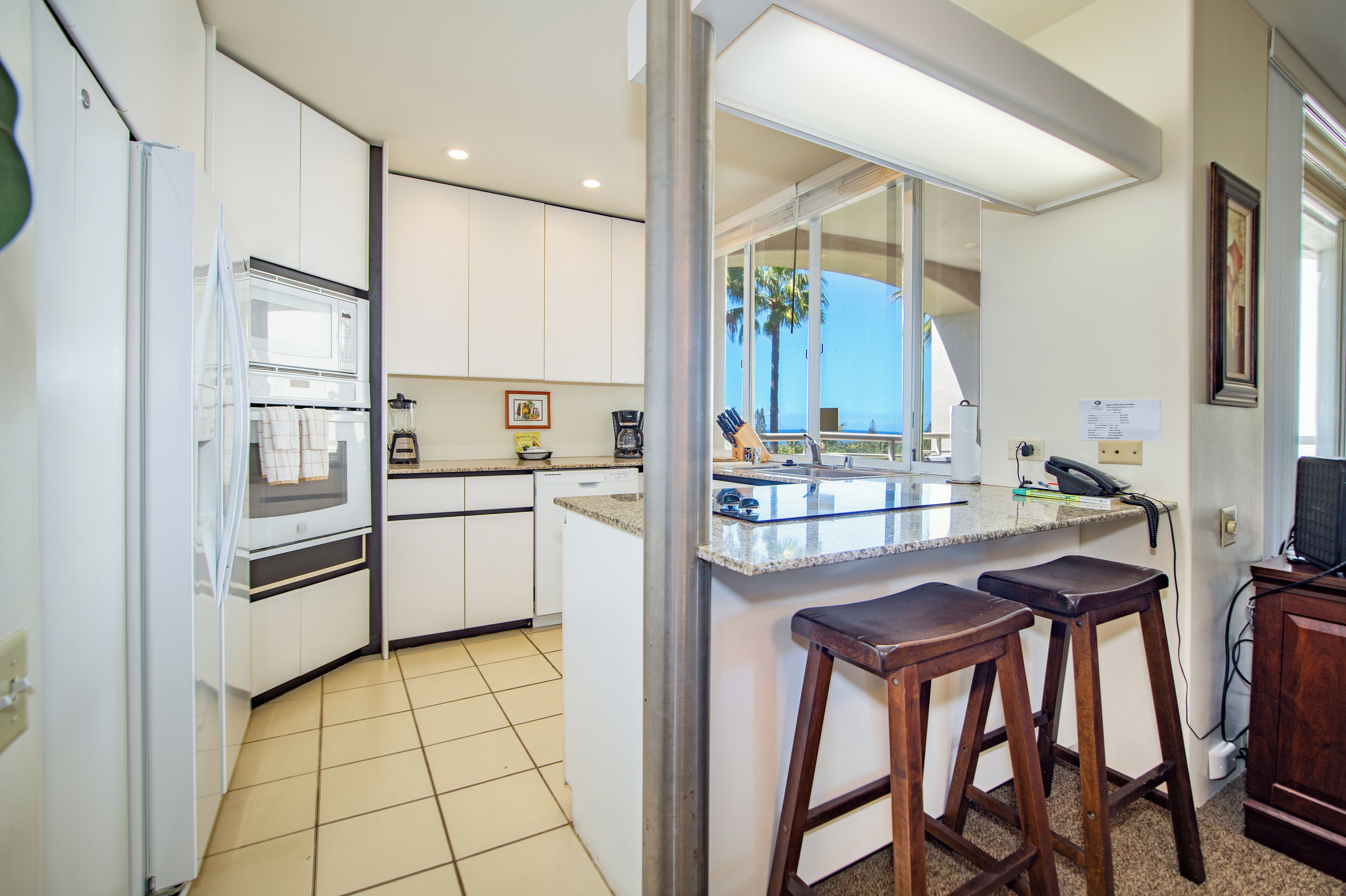 A kitchen with white cabinets, a microwave, a coffee maker, and a bar area with stools.