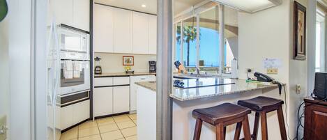 A kitchen with white cabinets, a microwave, a coffee maker, and a bar area with stools.