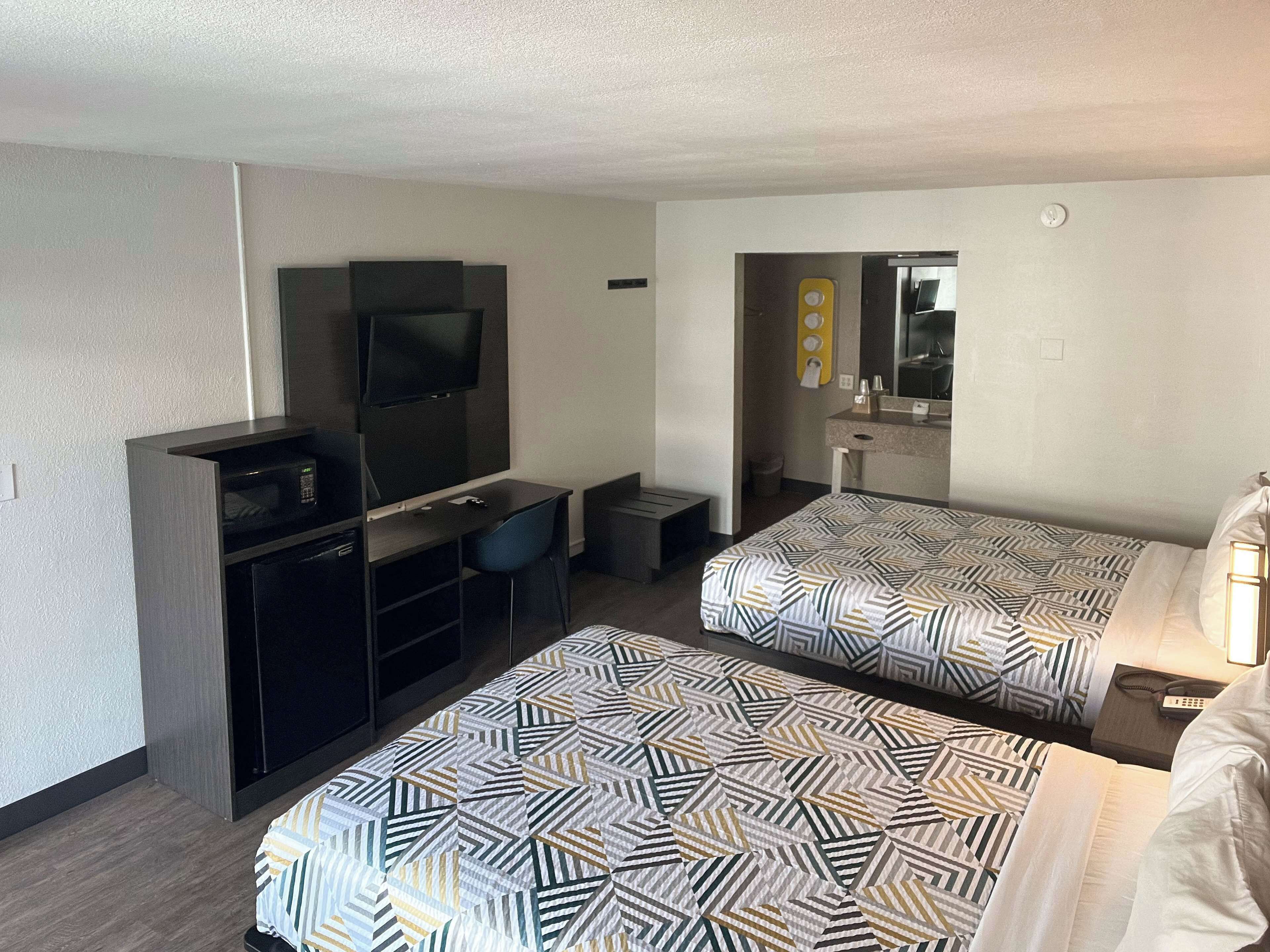 A hotel room with two single beds, a desk with a TV, a small bathroom, and a mirror.