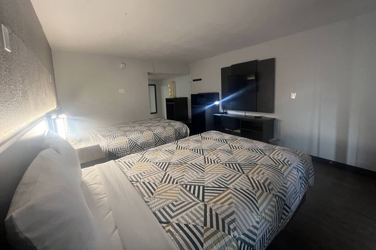 Hotellihuone, jossa on kaksi sänkyä, työpöytä, televisio ja peili.