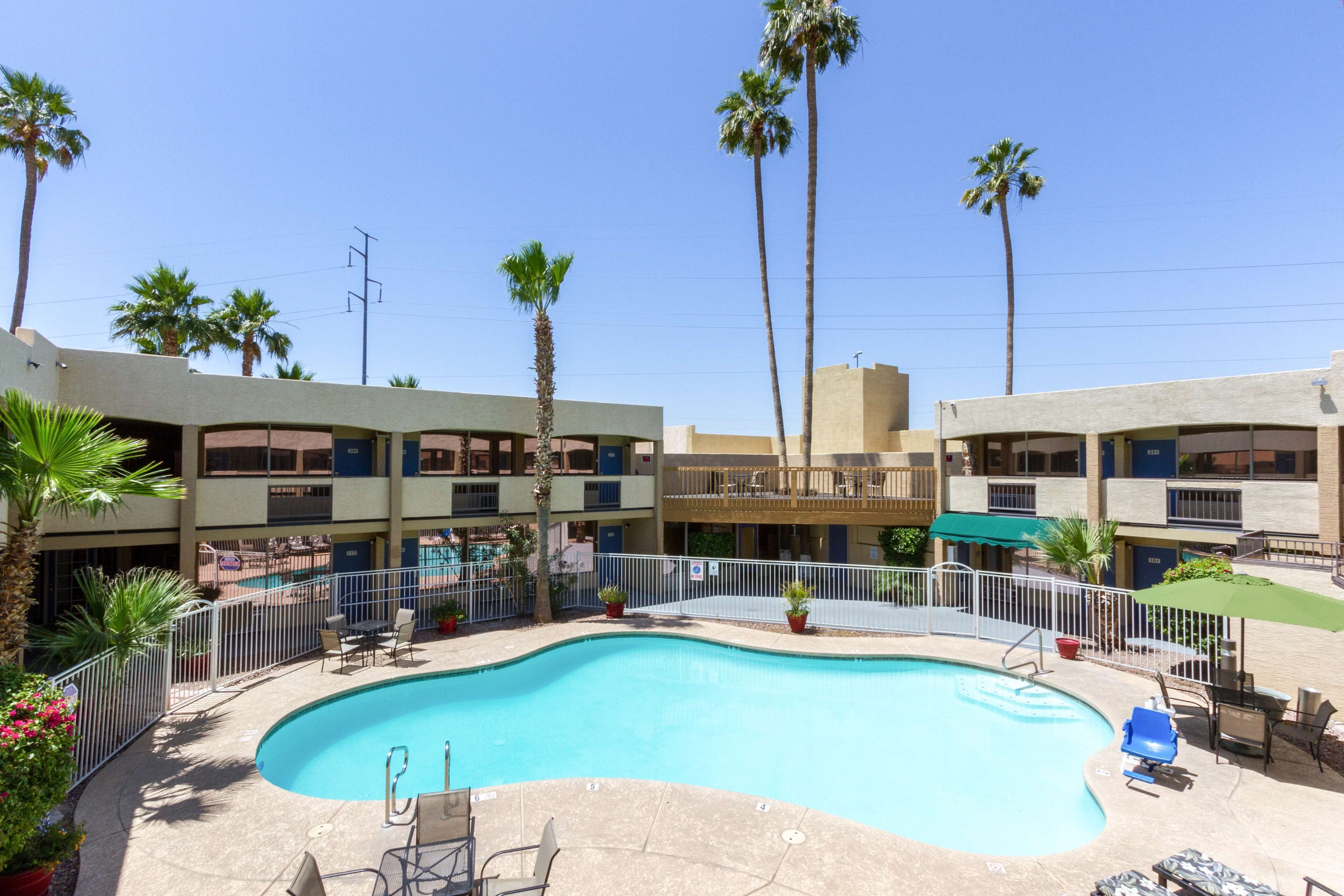 A hotel with a swimming pool, palm trees, and outdoor seating.