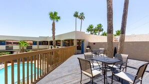 Un área junto a la piscina con cubierta de madera, asientos al aire libre y palmeras.
