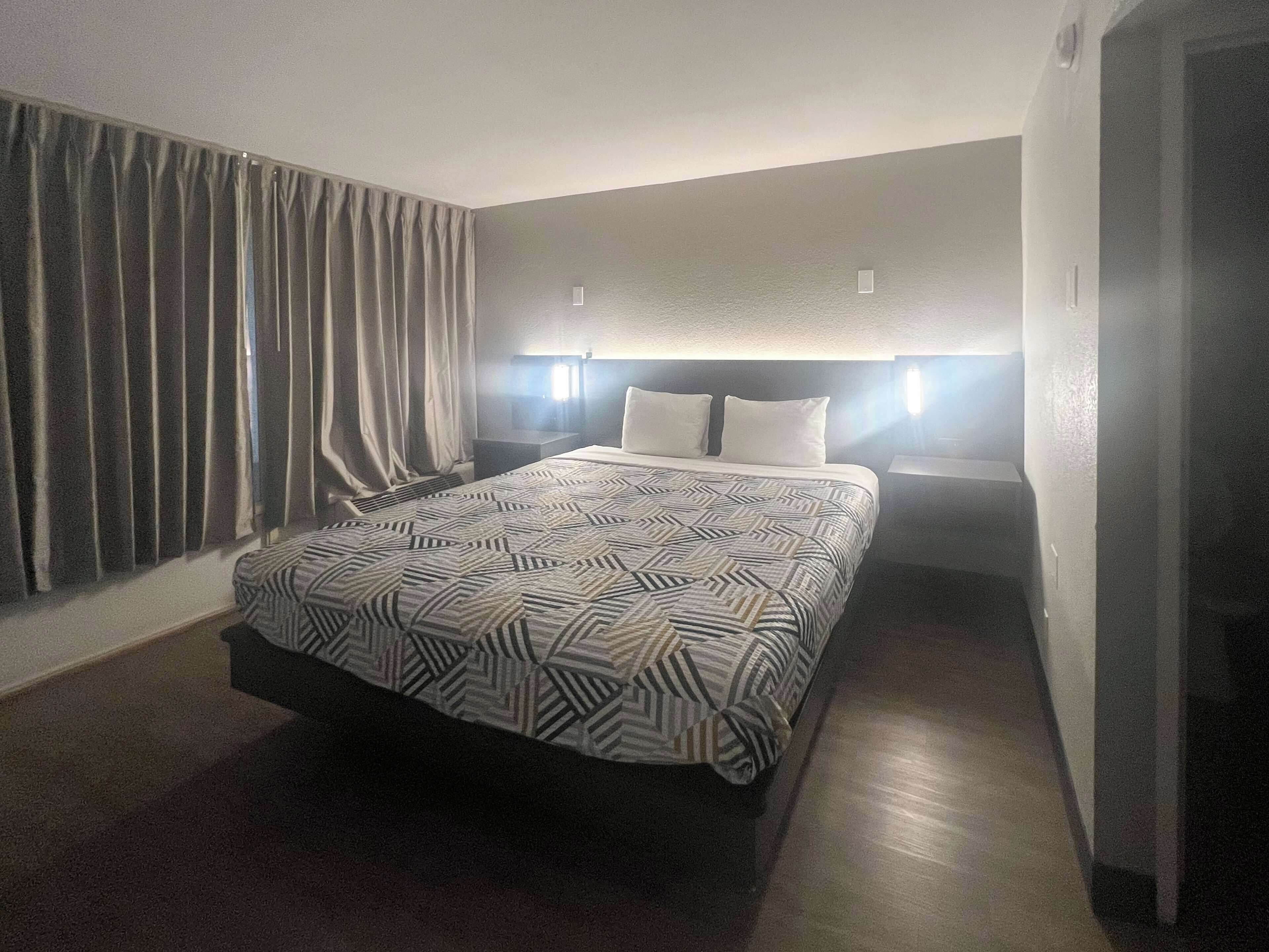 Une chambre d’hôtel avec un grand lit, deux tables de chevet, une tête de lit et une fenêtre avec des rideaux.