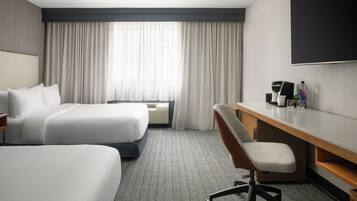 A hotel room with two beds, a desk with a chair, a flat-screen TV, and a coffee maker.