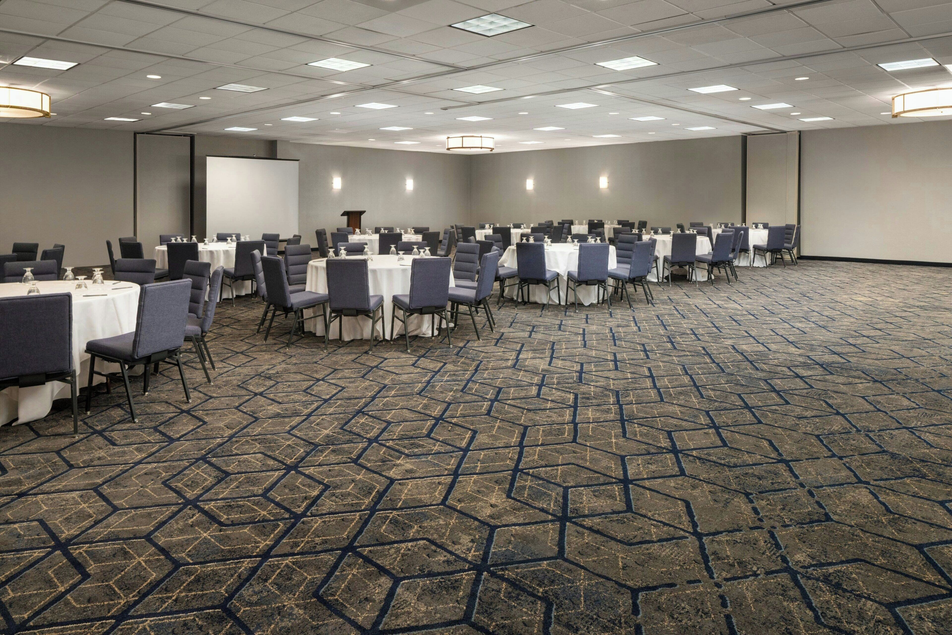 A conference room with rows of tables and chairs, a projector screen, and a podium.