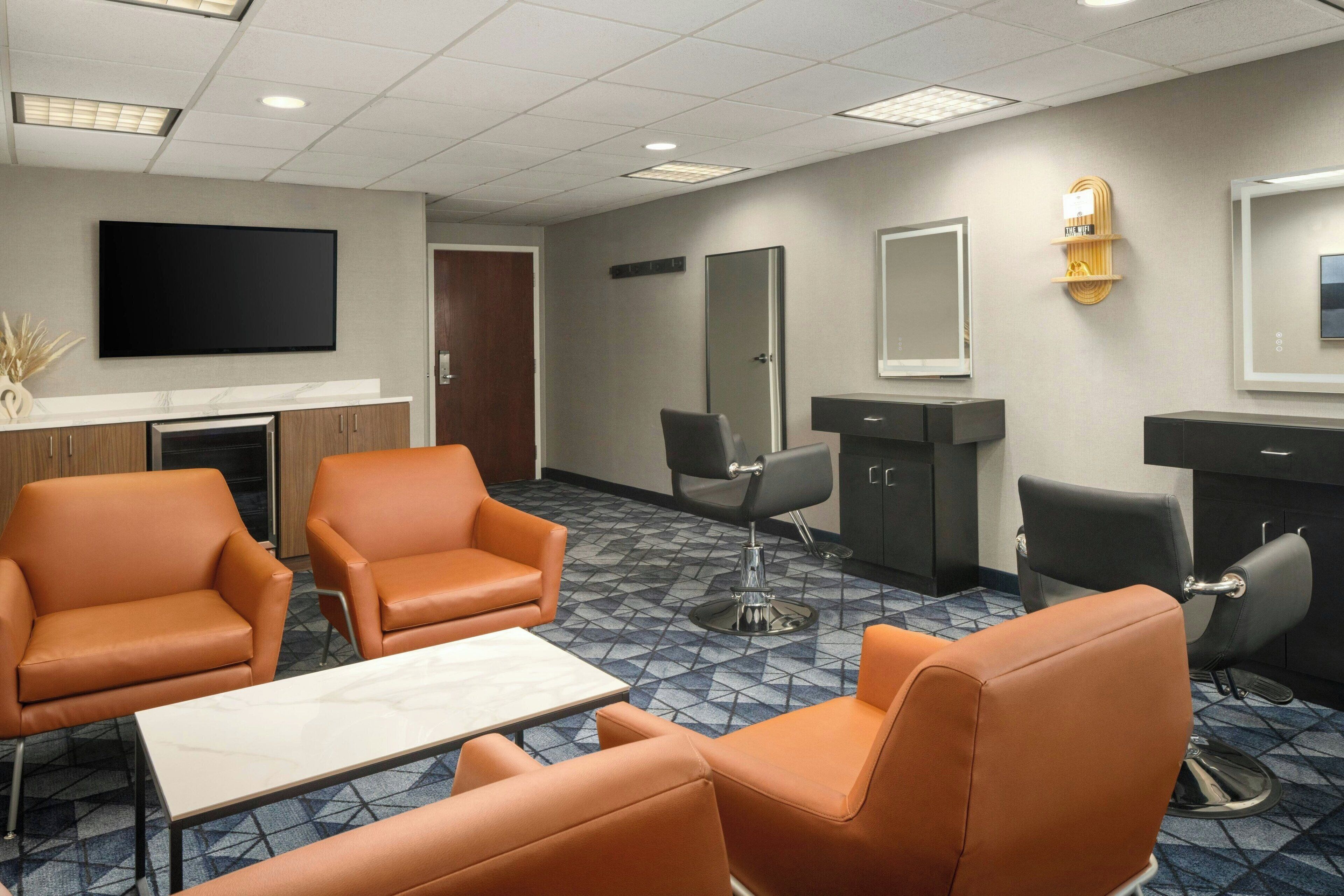 A hotel room with a large flat-screen TV, a sofa, a table, and a mirror.