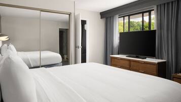 Una habitación de hotel con una cama, un televisor sobre un aparador de madera y un espejo grande.