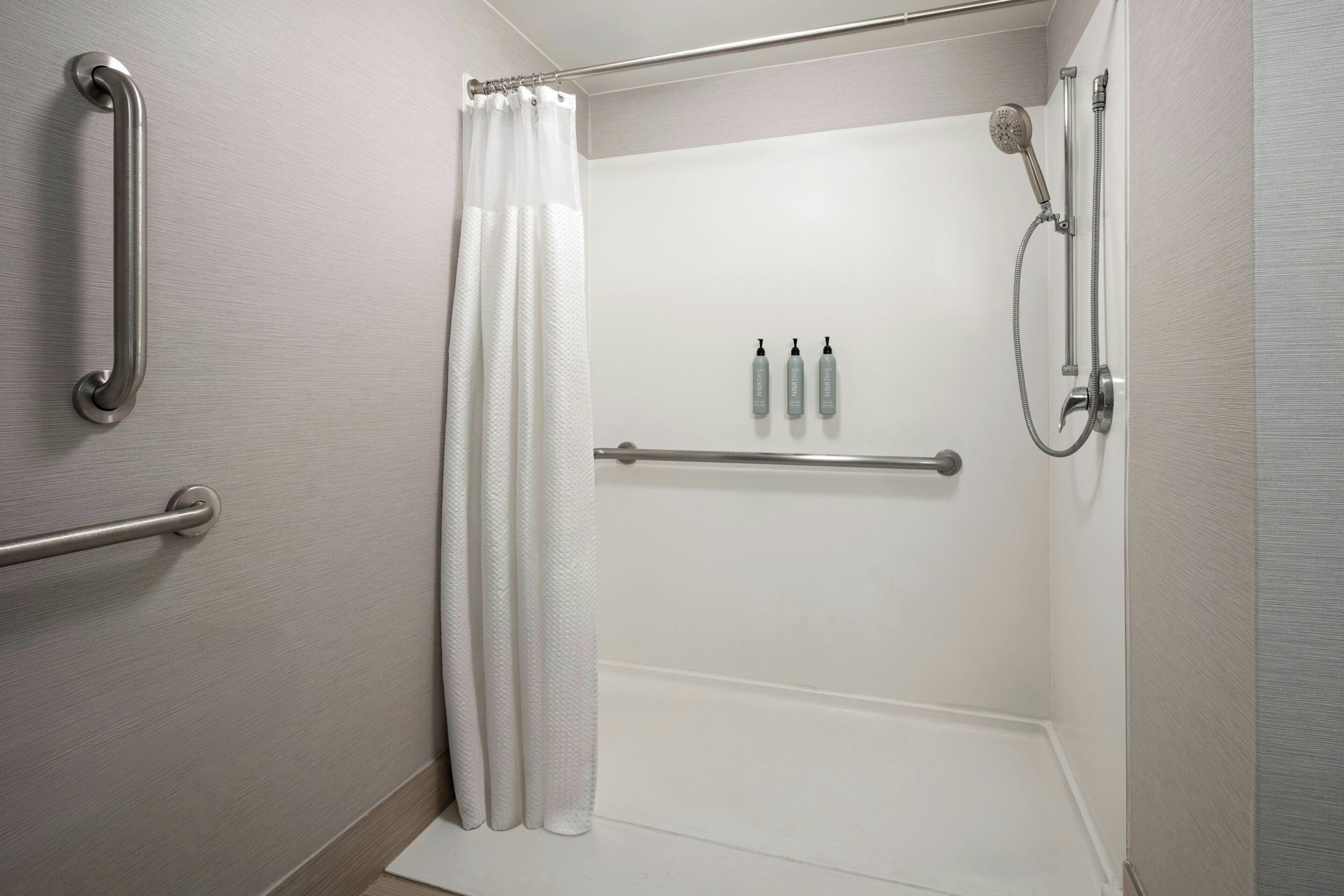 Une salle de bain équipée d’une douche, de barres d’appui, d’un porte-serviettes et d’un rideau.
