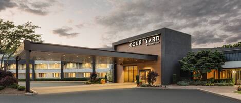 A modern hotel entrance with a covered driveway, a sign reading "Courtyard by Marriott," and a well-lit facade.