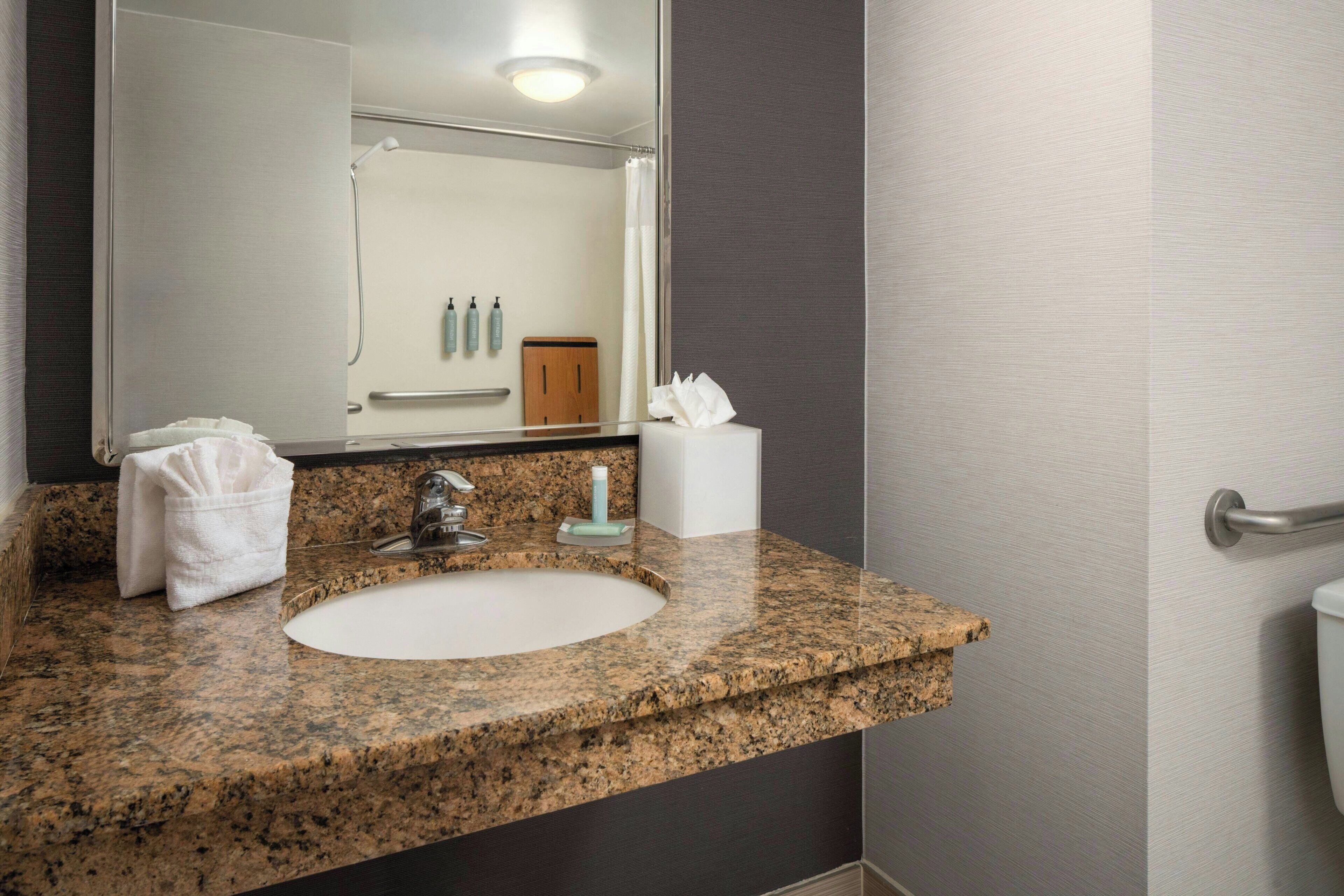 A bathroom with a granite countertop sink, a mirror, a towel, and a toilet.